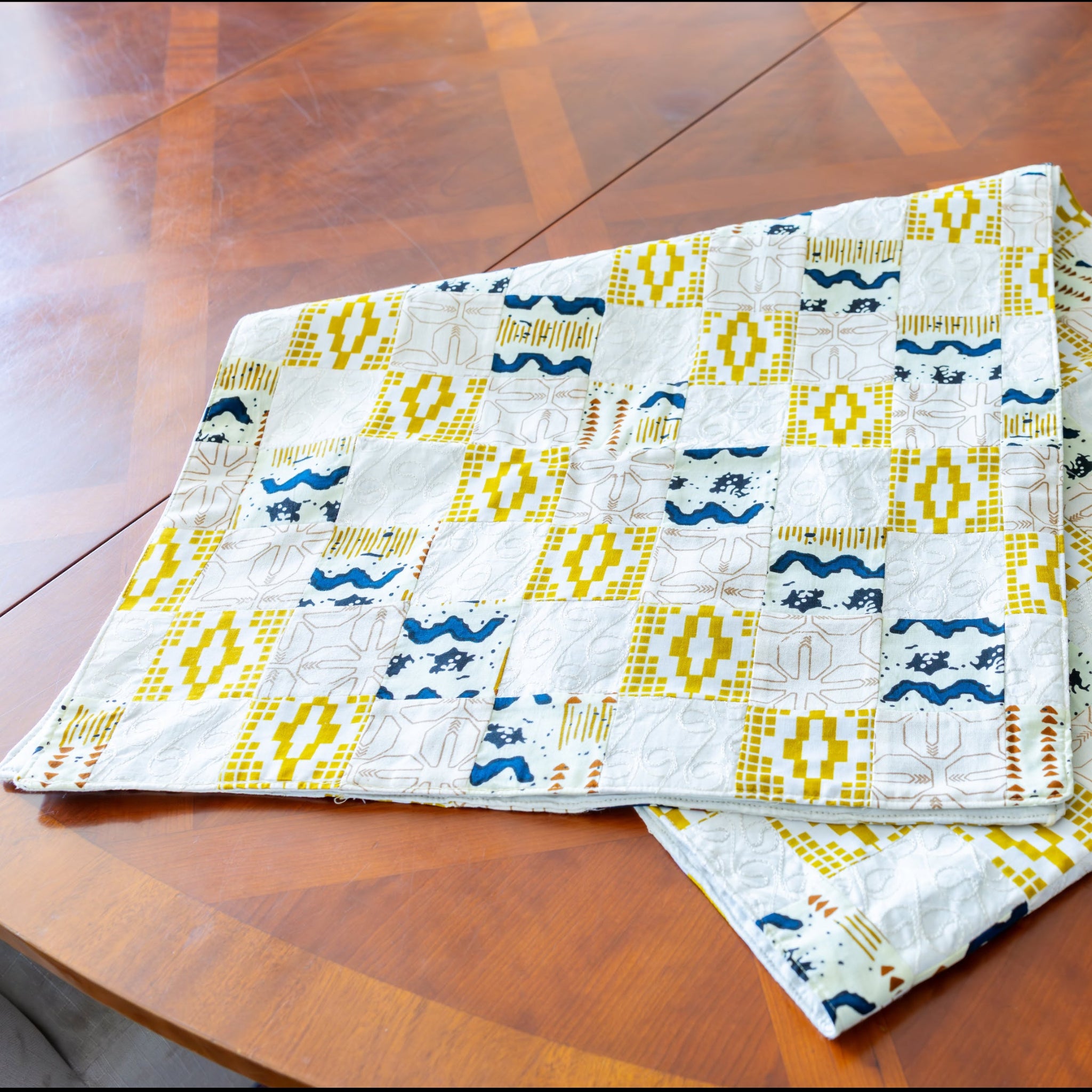 folded gold, blue, and white patchwork table runner on a wooden table