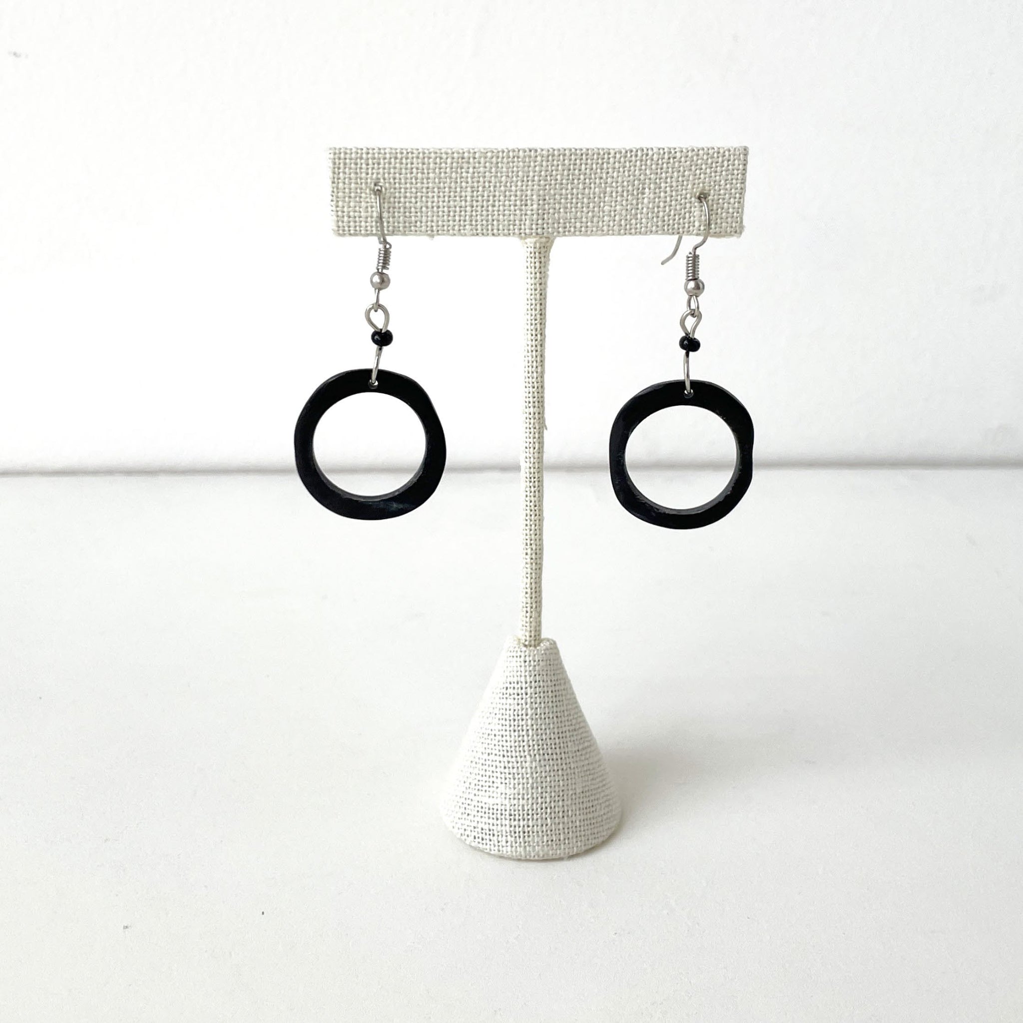 Black circular earrings on a textured earring stand against a white background