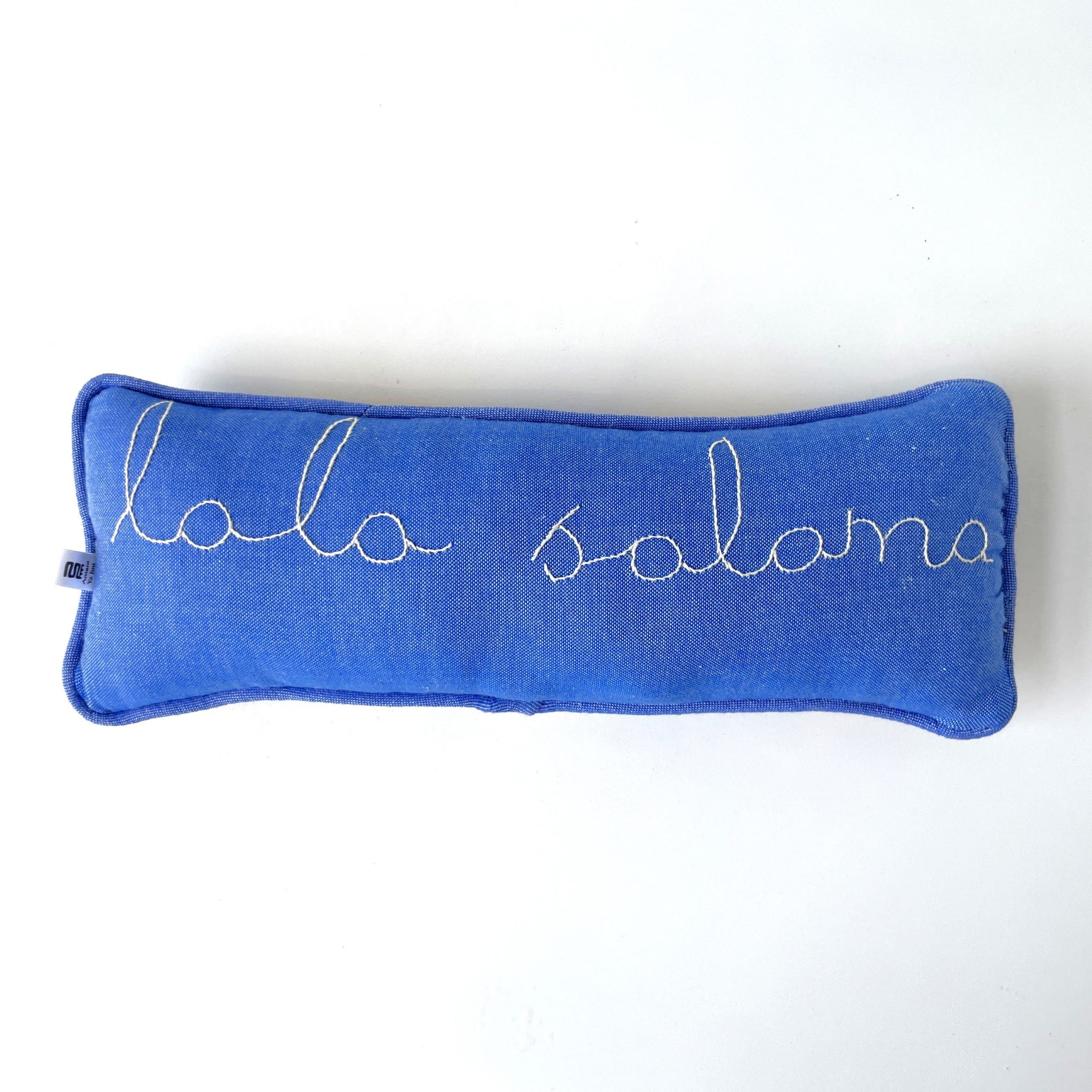 Blue pillow with 'lala salama' embroidery on a white background