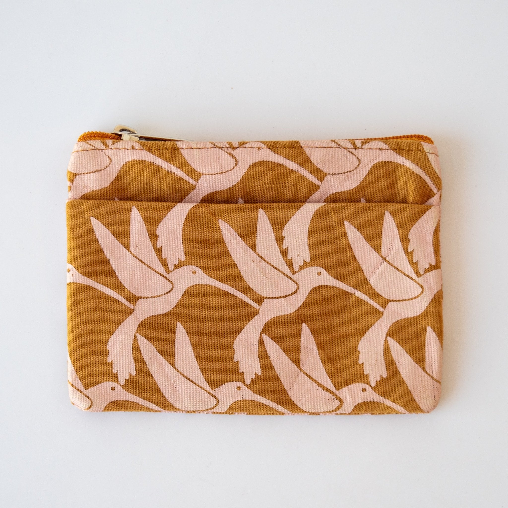 Caramel colored coin purse with pink hummingbird pattern on a white background.