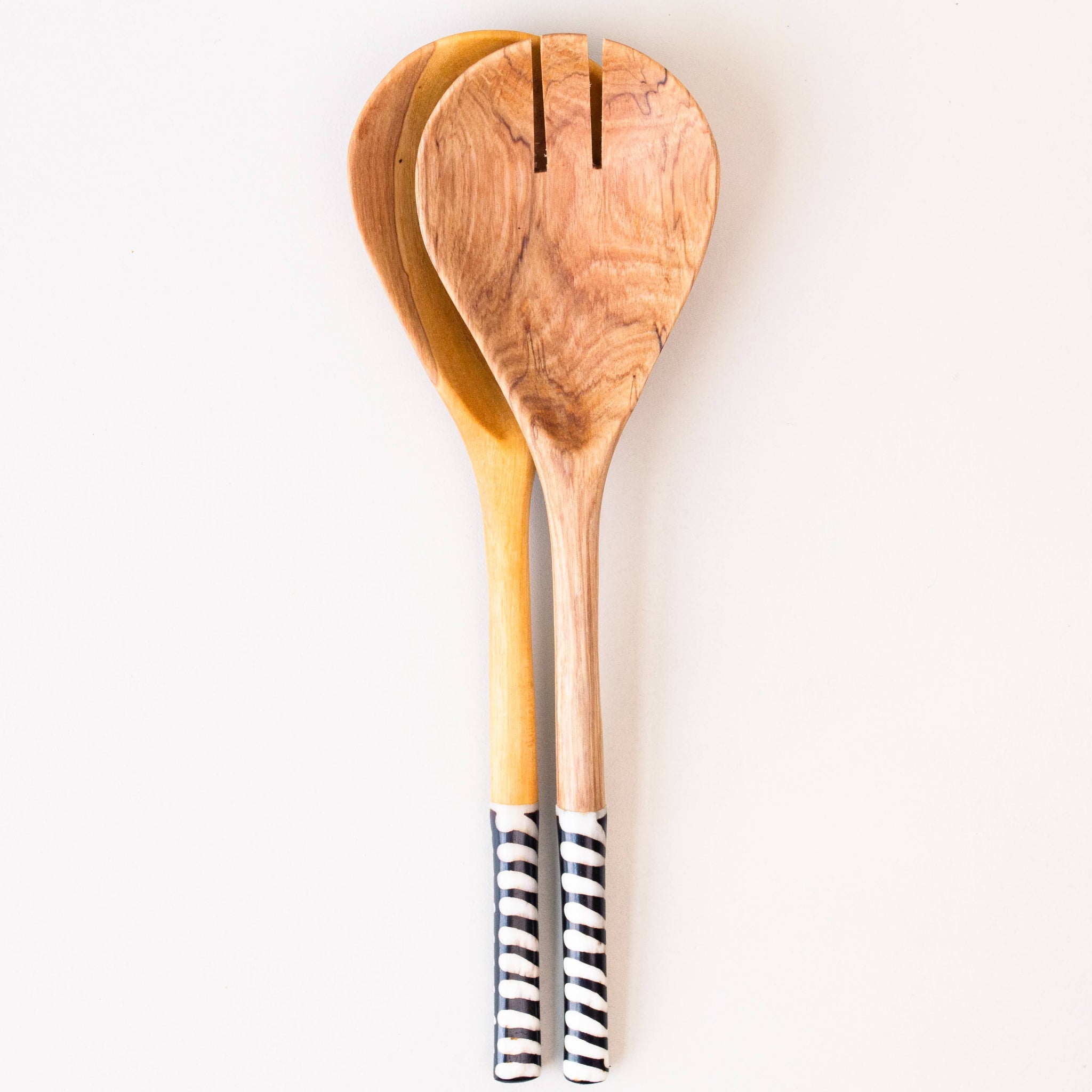 Two wooden salad or serving spoons with black and white striped handles, arranged vertically on a plain white background.