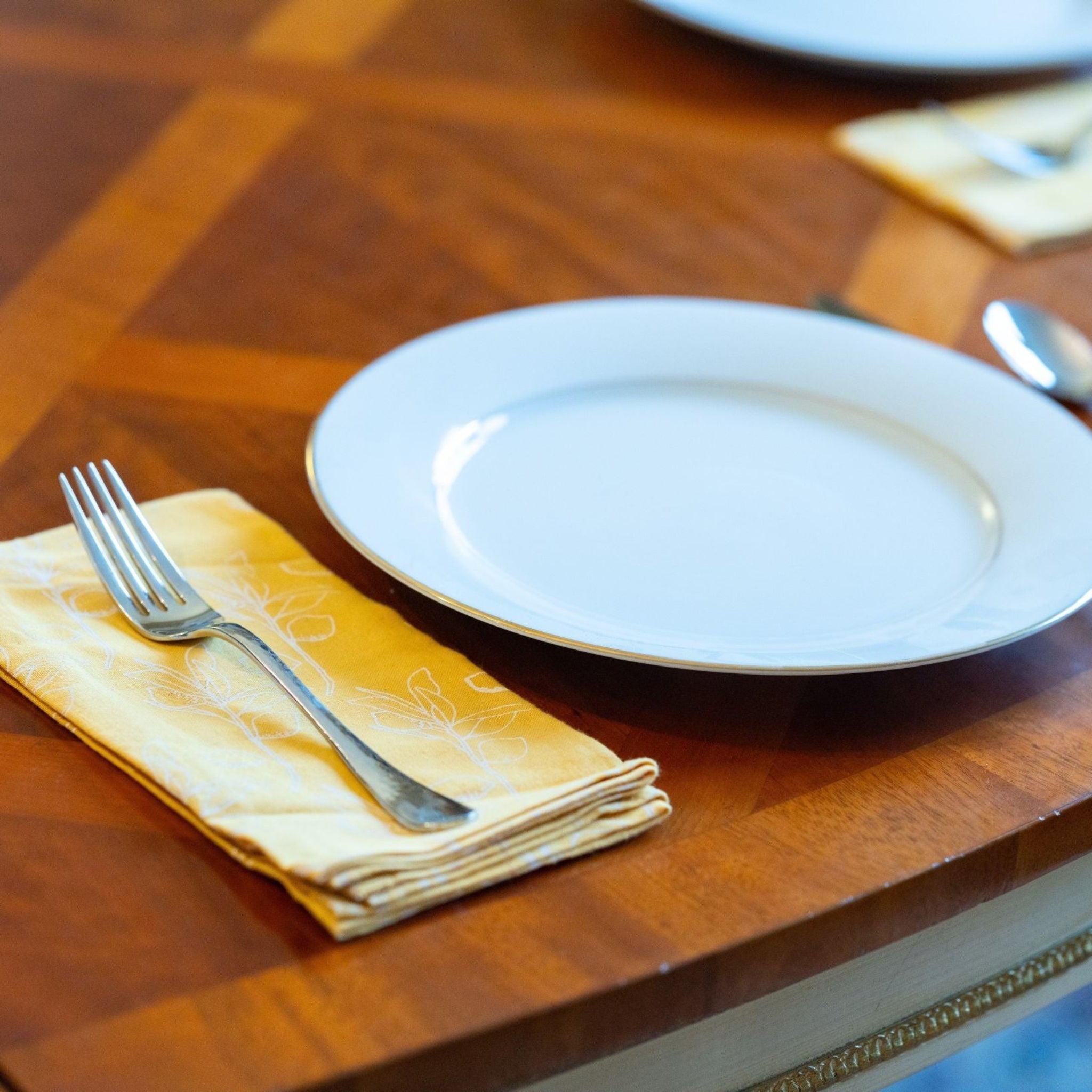 Dining table setting with a white plate, fork, and spoon on a wooden surface.