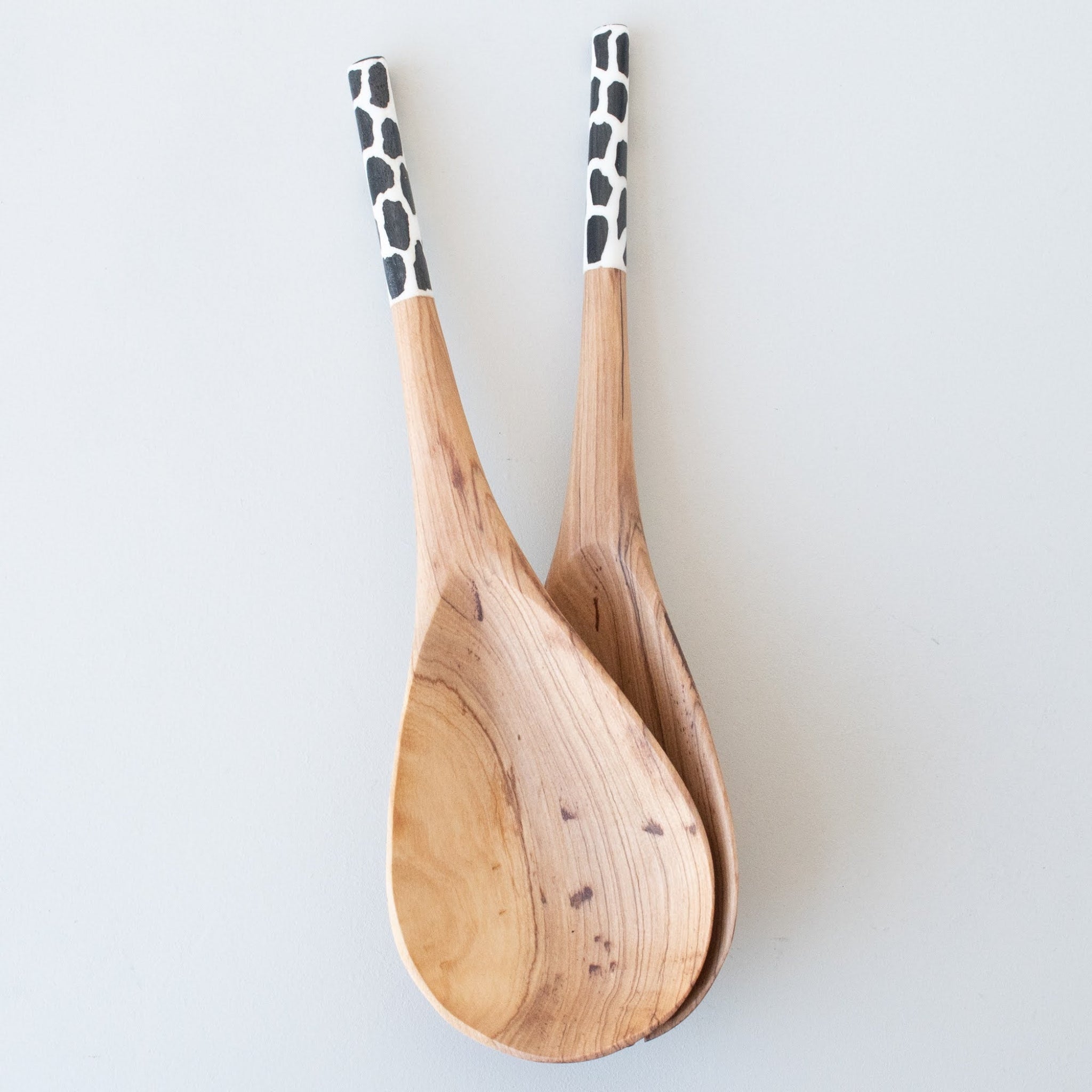 Two wooden salad spoons with black and white spotted handles, arranged overlapping on a light gray background.