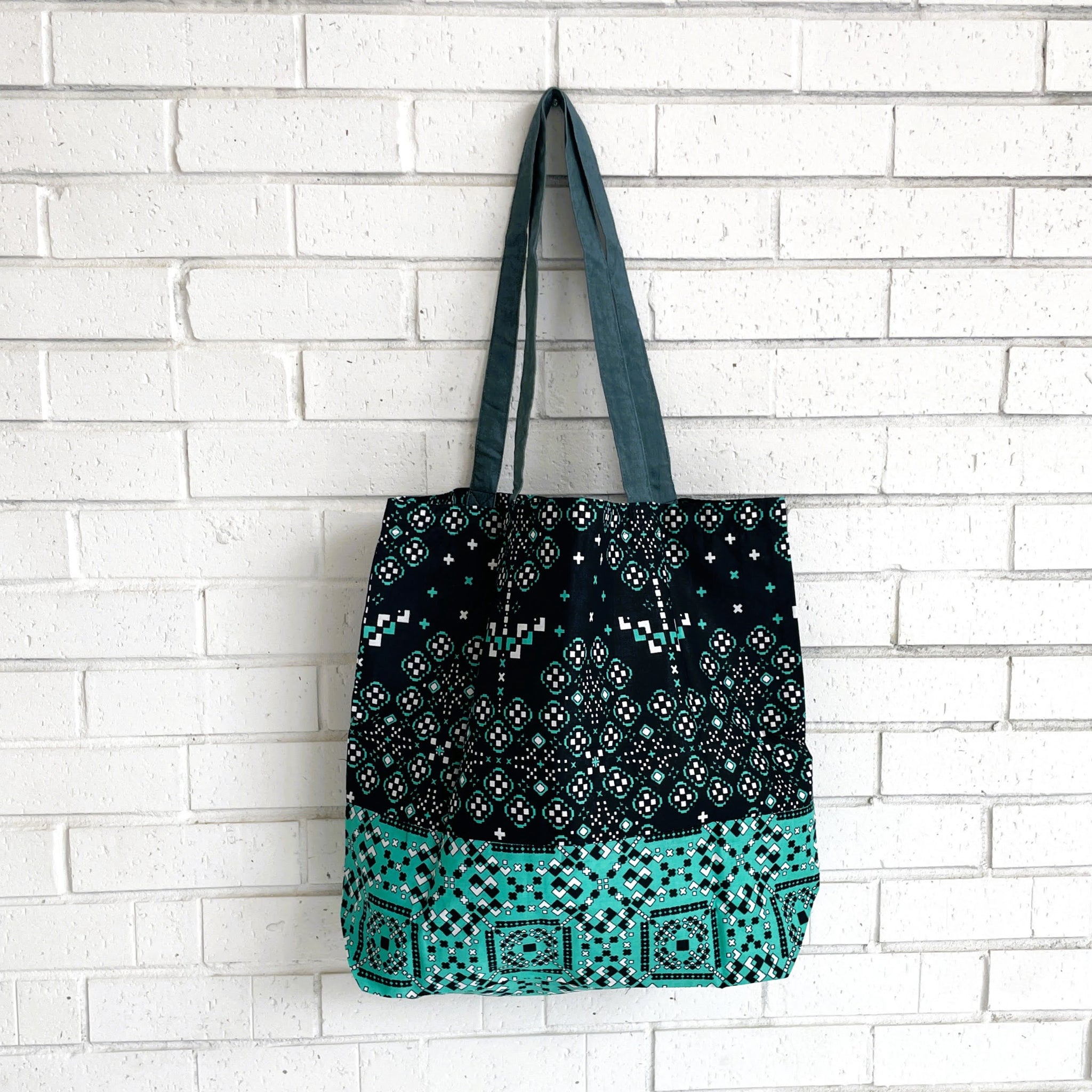 Tote bag with navy and turquoise pattern against a white brick wall