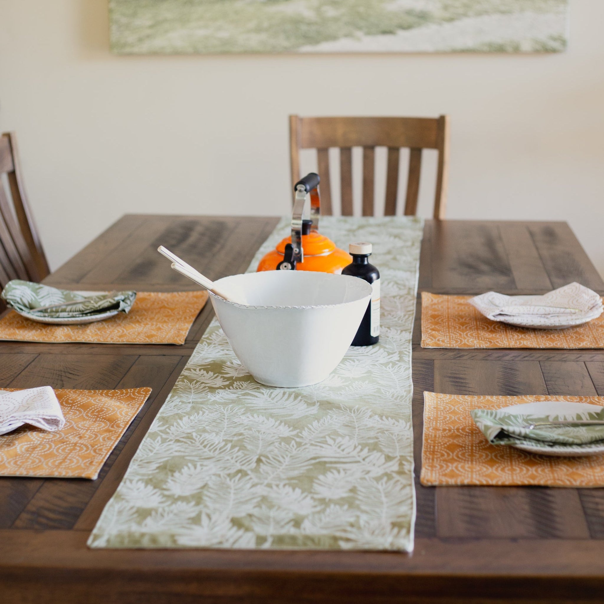 Dining table setting with a white bowl, patterned placemats, table runner, and napkins.