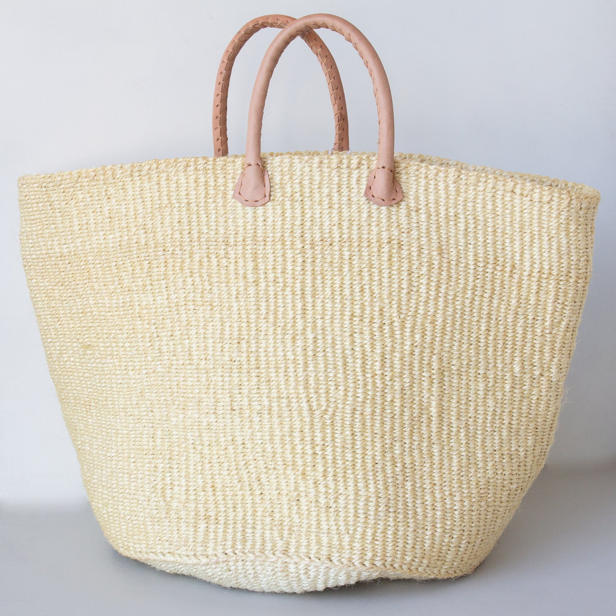 Woven sisal tote bag with leather handles on a light gray background