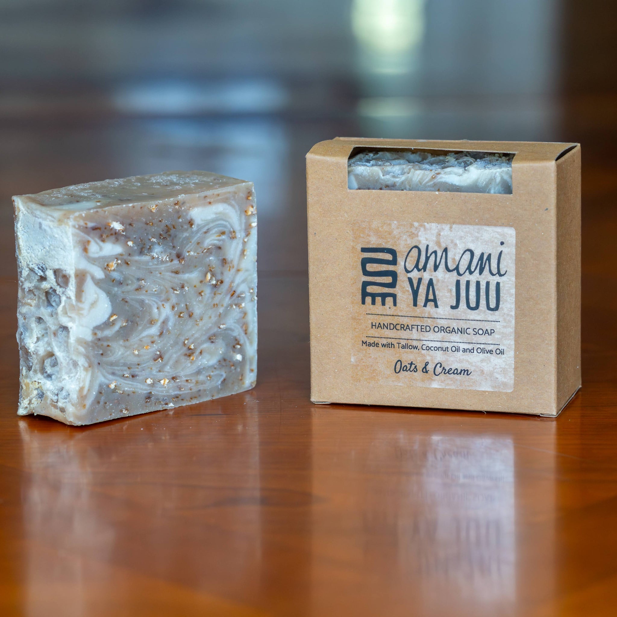 A handmade soap bar with a marbled white and gray pattern and gold glitter flecks, shown next to its kraft paper packaging box on a polished wooden table.