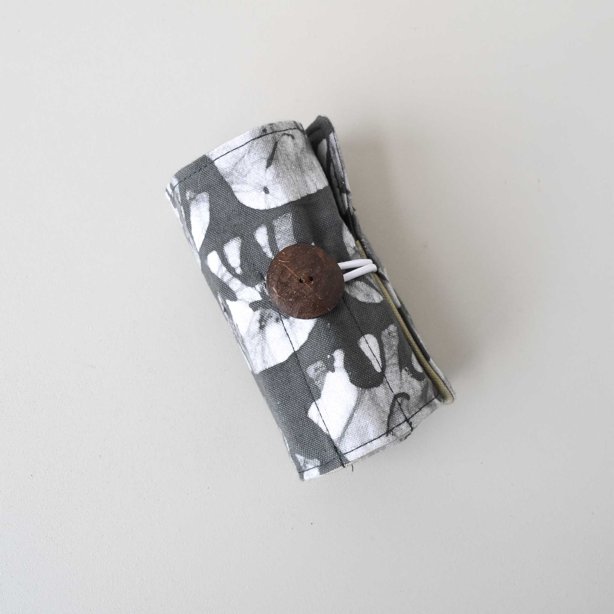 Fabric crayon holder pouch rolled and buttoned on a light gray background