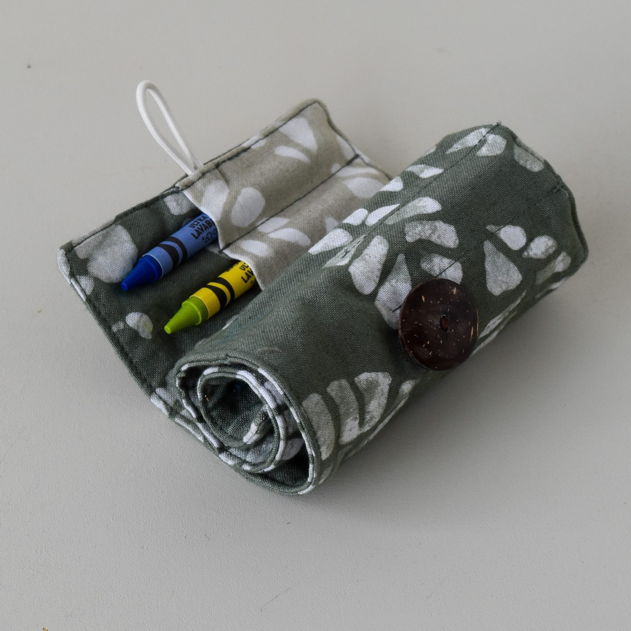 Fabric crayon holder pouch with button and tag on a light gray background