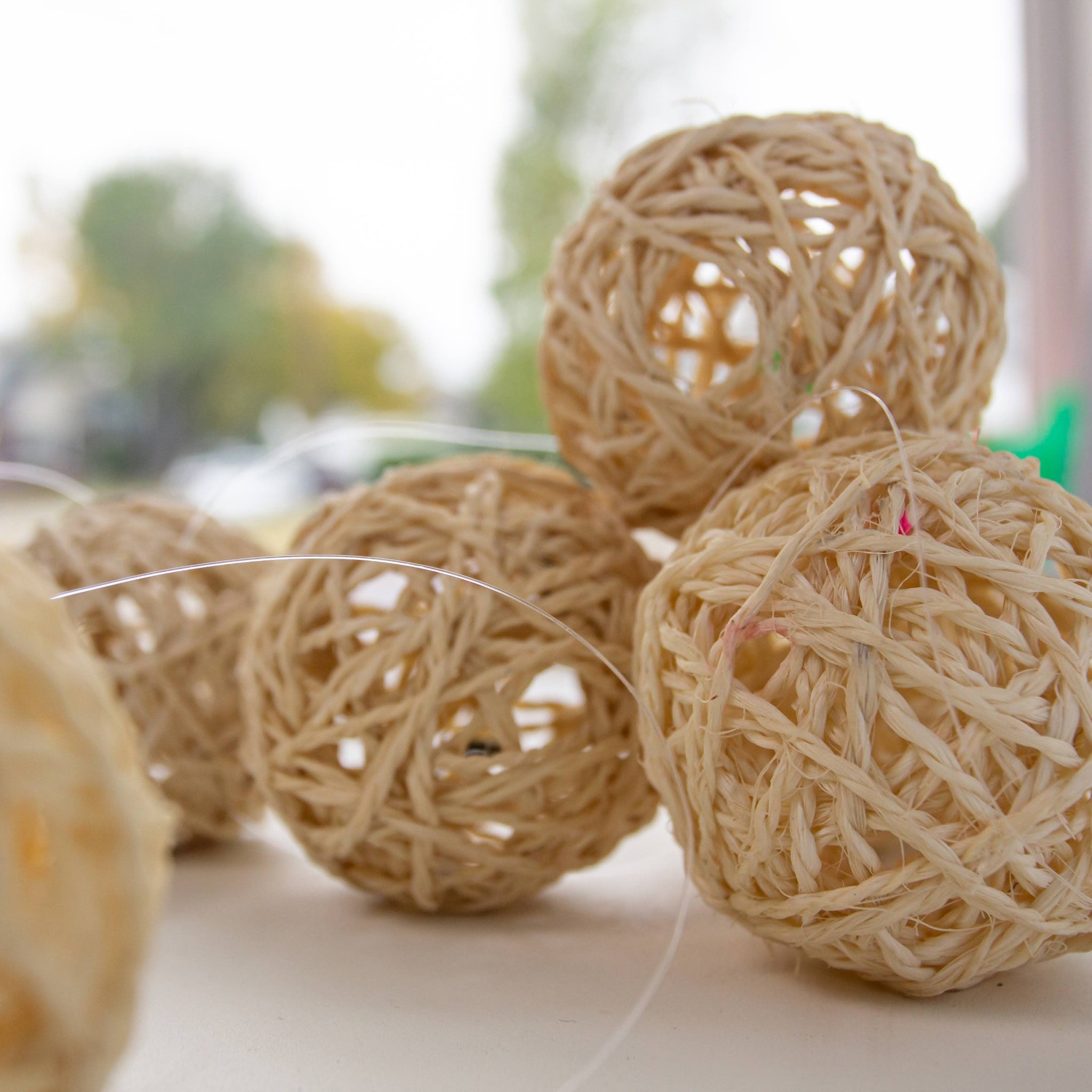 Three woven sisal balls on a light surface with a blurred natural background