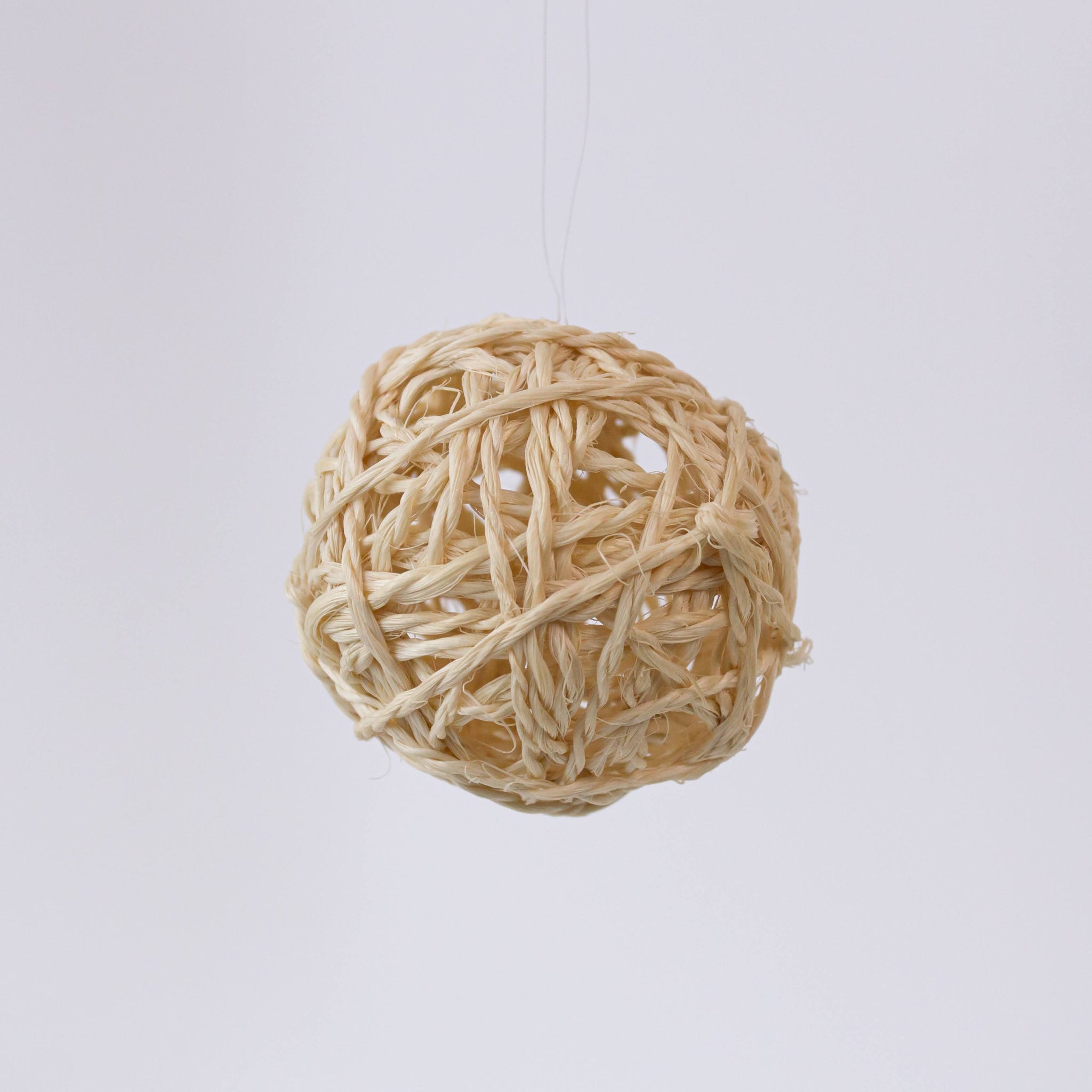 A beige sisal ball ornament handmade from sisal grass, displayed against a blurred background.