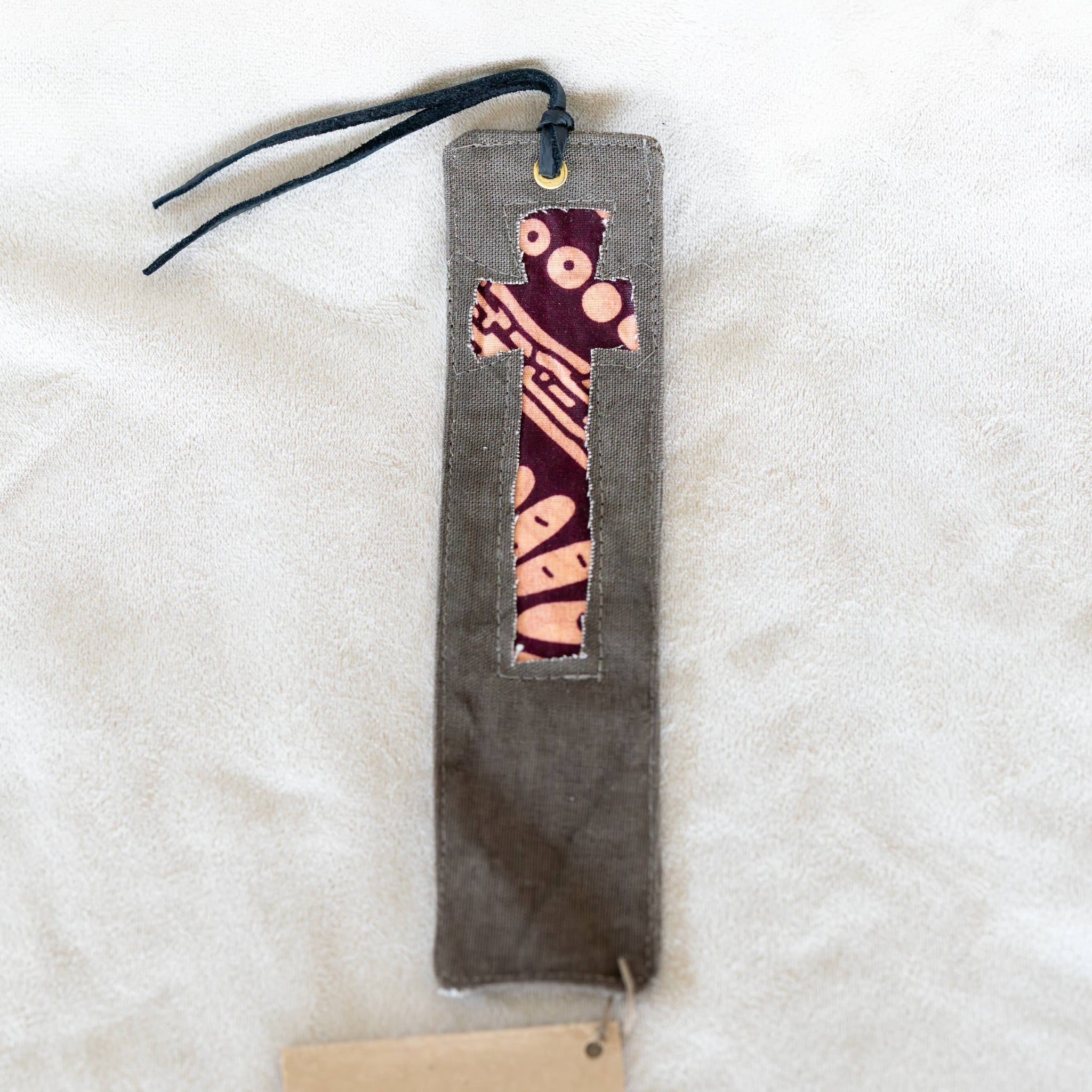 A handmade bookmark featuring a dark gray fabric body with a decorative pocket containing a pink and purple patterned fabric strip. A black cord is attached at the top,