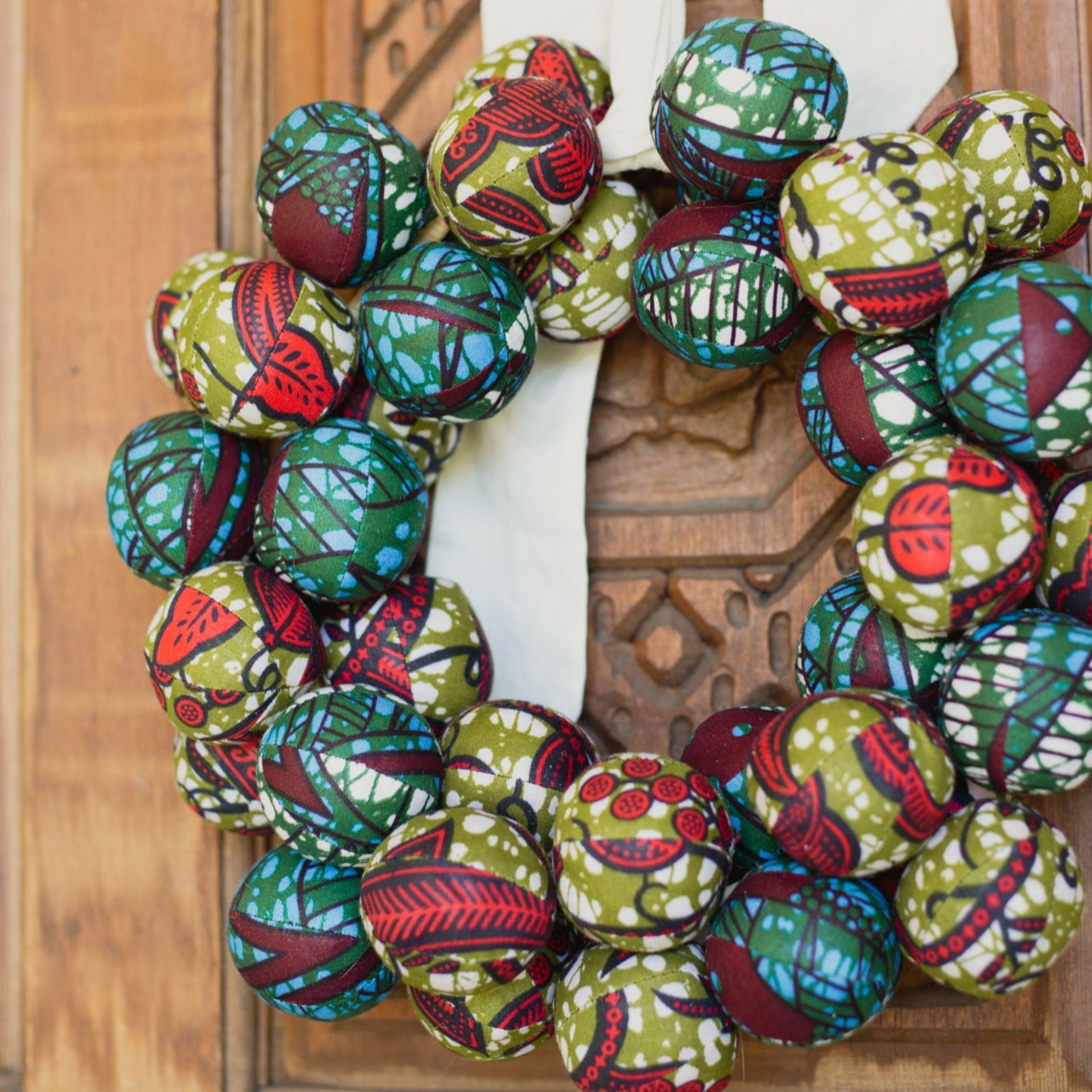 Decorative wreath made of colorful fabric balls hanging on a wooden door.
