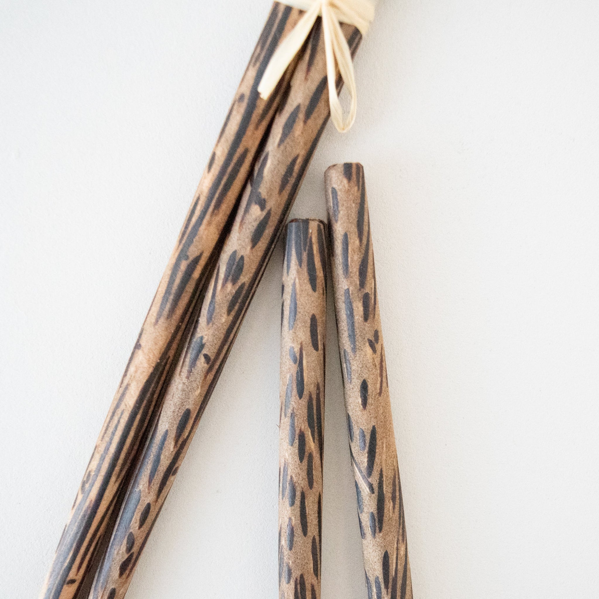 Four wooden chopsticks with a dark brown leopard print pattern on a light natural wood base, tied together with a beige string at the top, set against a plain white background.