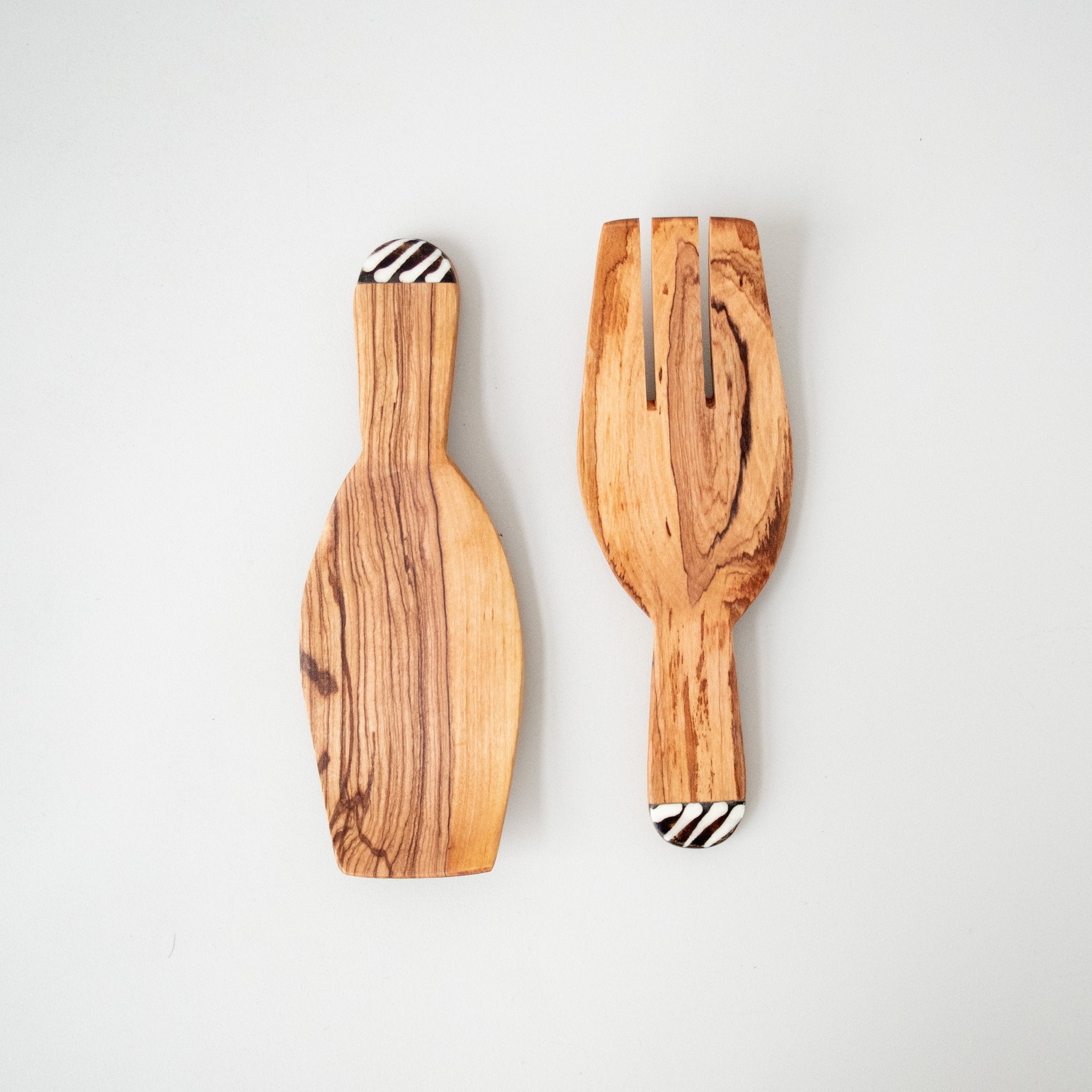 Two wooden salad spoons with bone inlay on the handles, placed on a white surface.