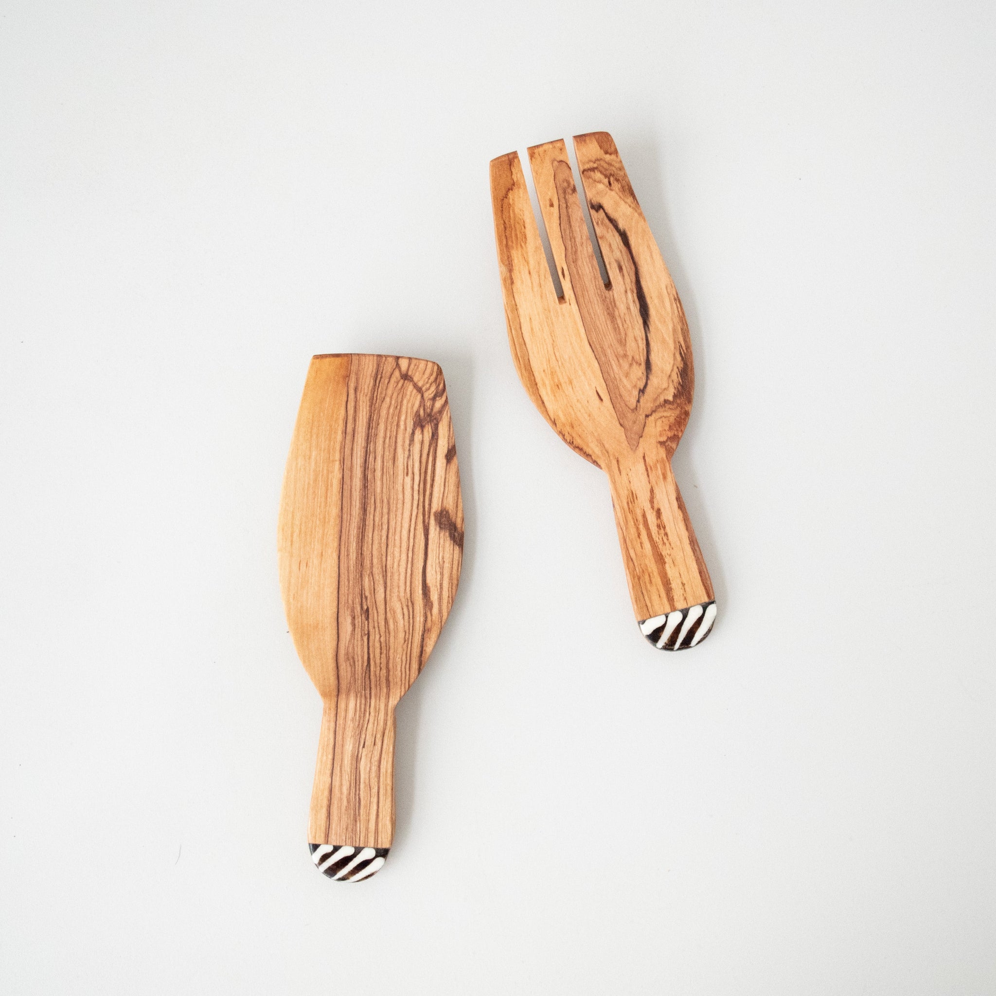 A set of two olivewood salad spoons with cow bone inlay, lying on a white surface.