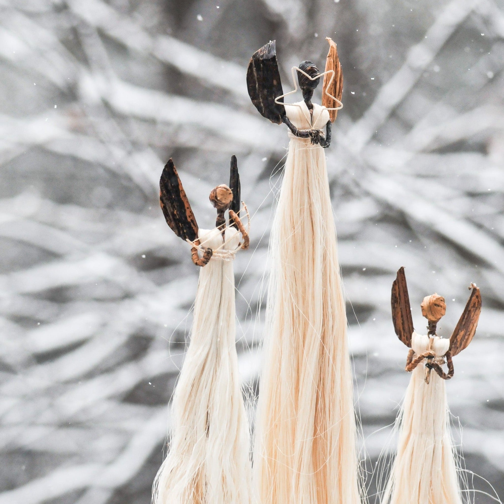 A set of three handcrafted sisal angel figures standing against a snowy backdrop.