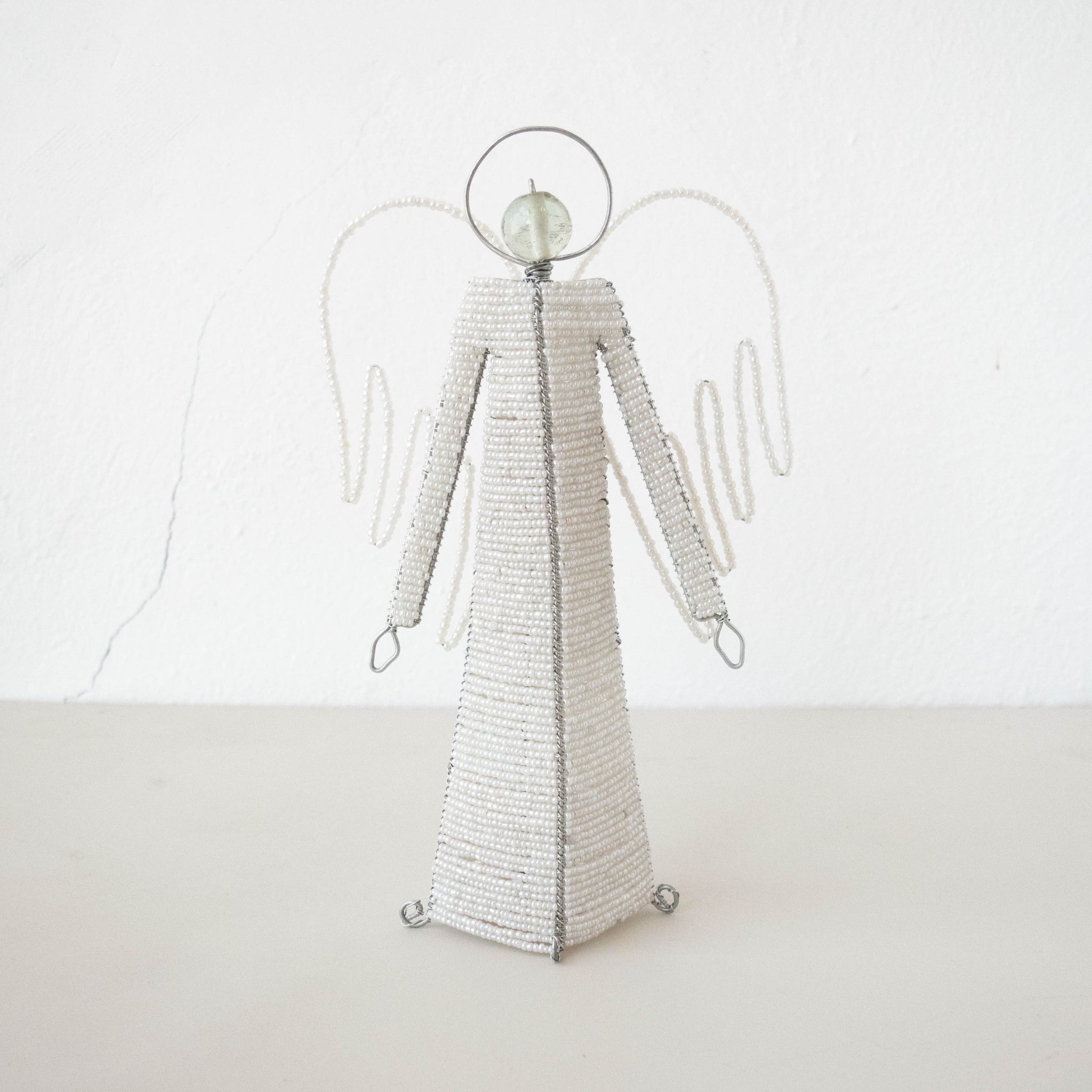A standing beaded angel figurine with a with silver accents, on a plain background.