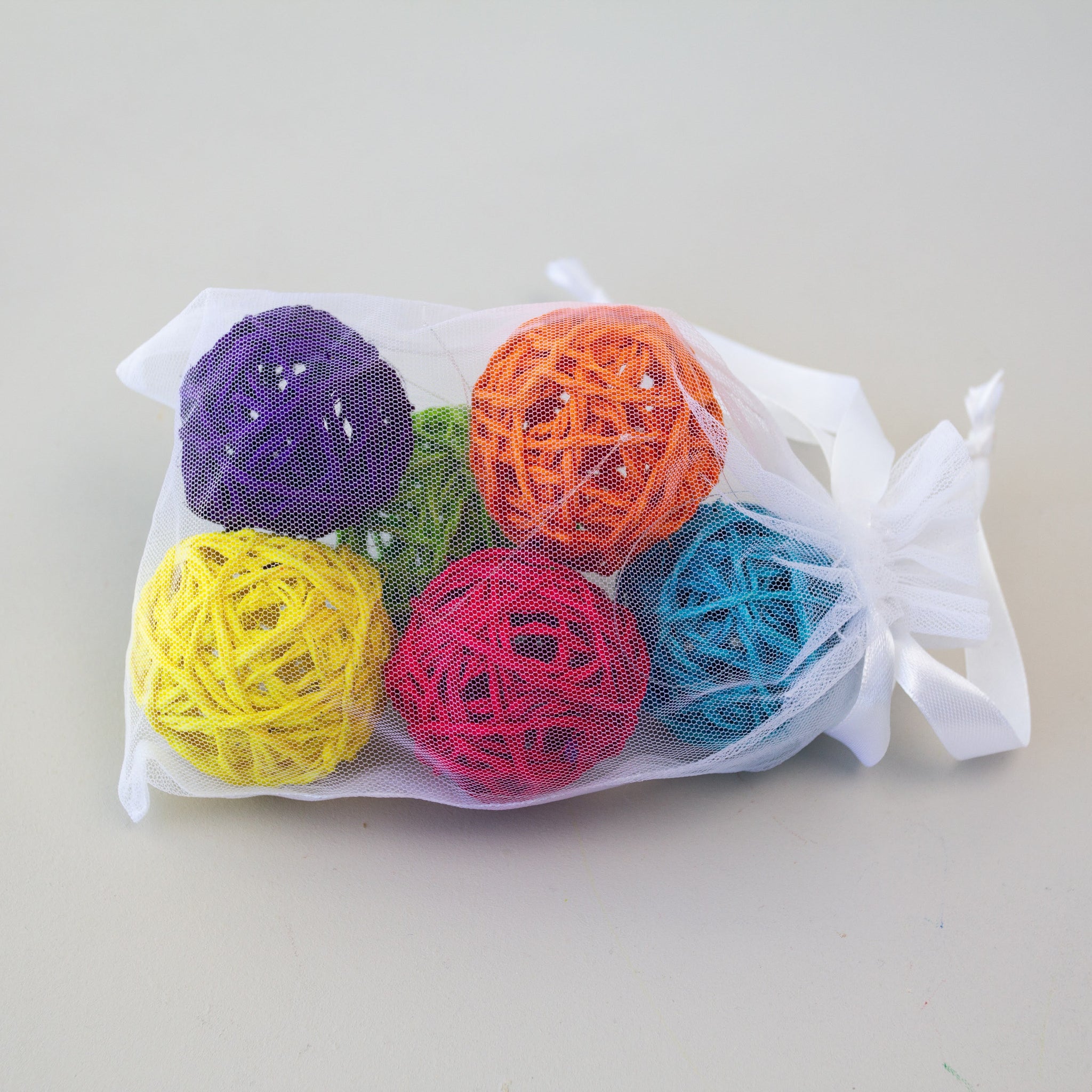 Set of colorful sisal balls in a mesh bag on a light gray background