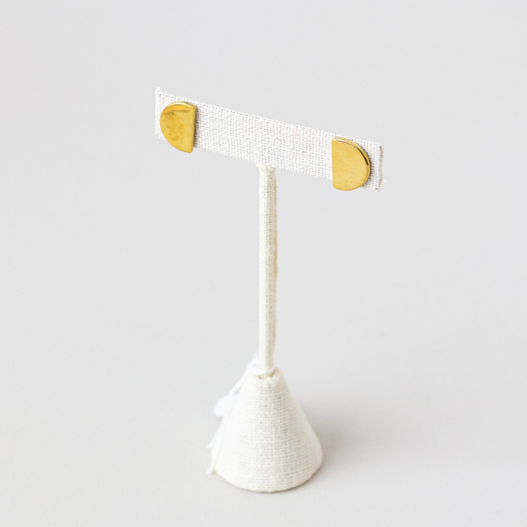 A pair of gold-colored, semi-circle shaped stud earrings displayed on a white stand.