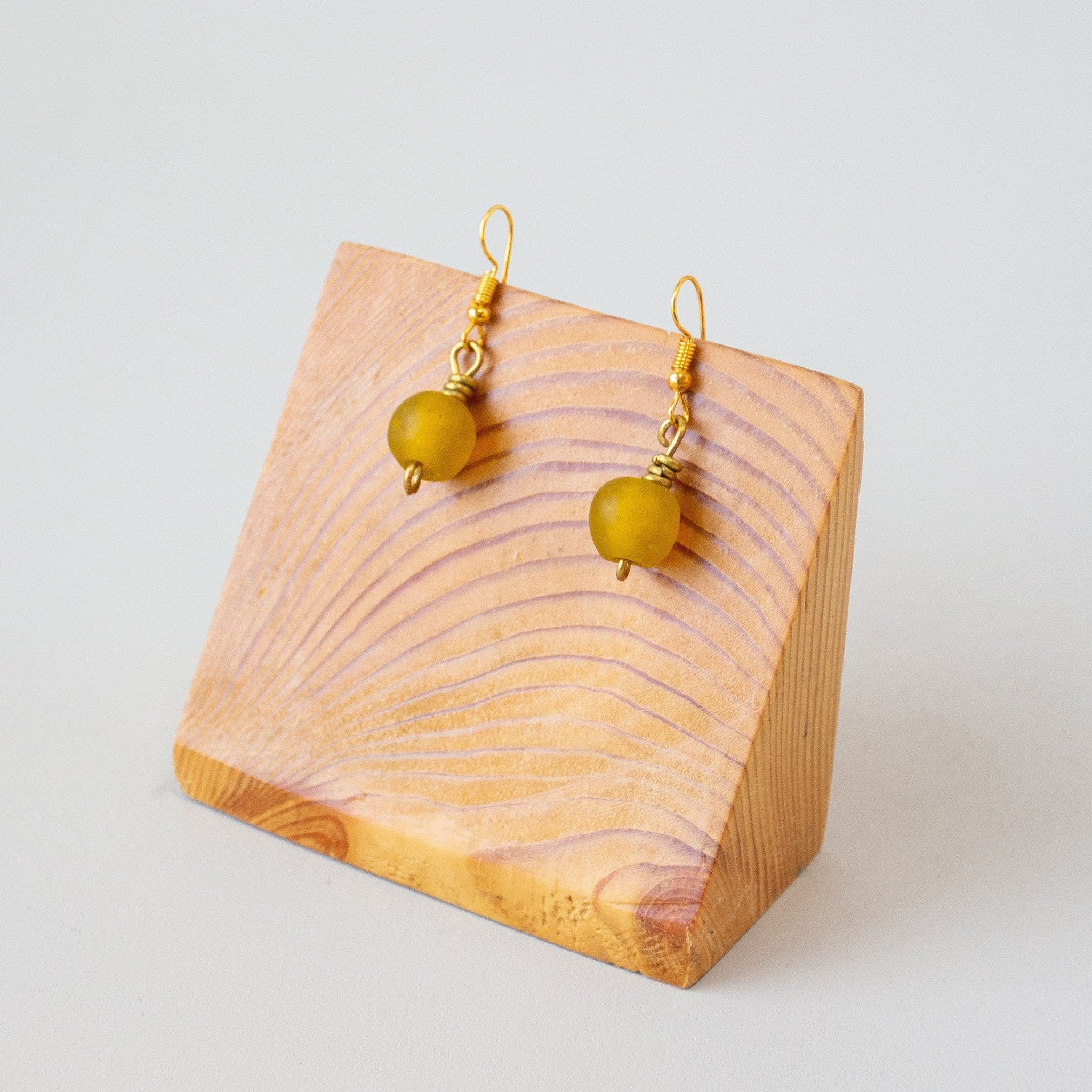 A pair of gold-tone dangle earrings with round translucent yellow beads, displayed on a small wooden stand against a light gray background.