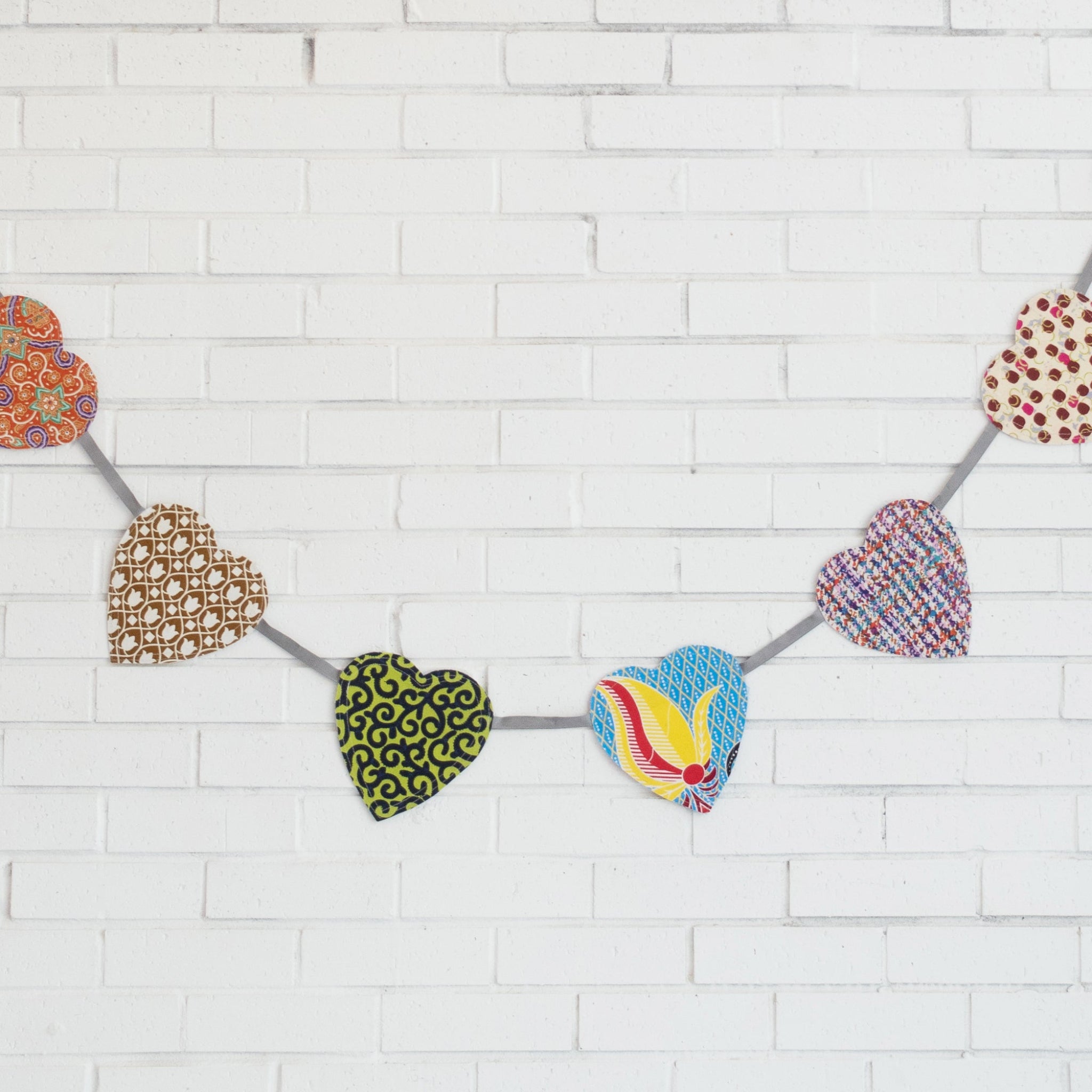 Decorative heart-shaped flags on a string against a white brick wall background