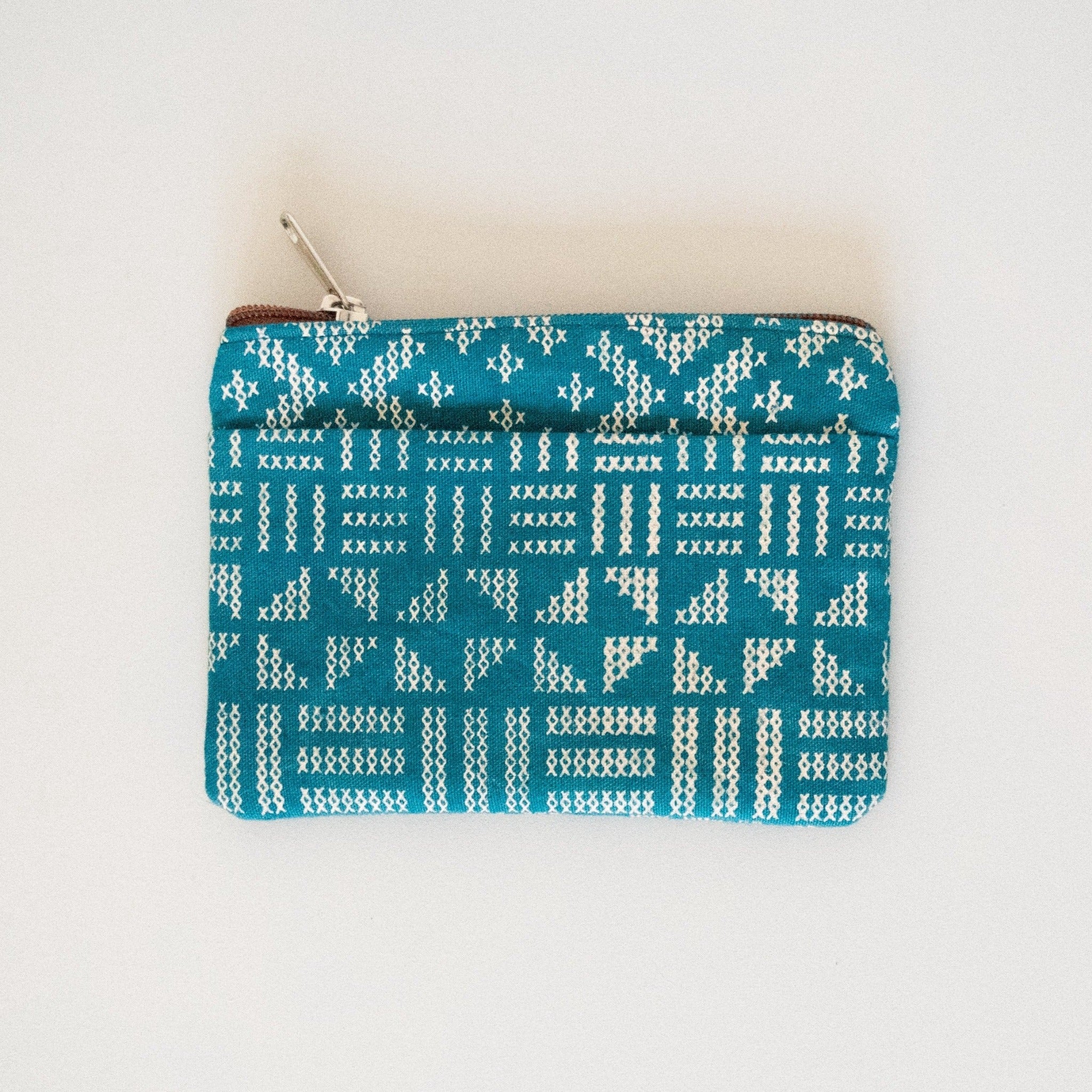 Teal colored coin purse with a cross-stitched pattern on a white background.