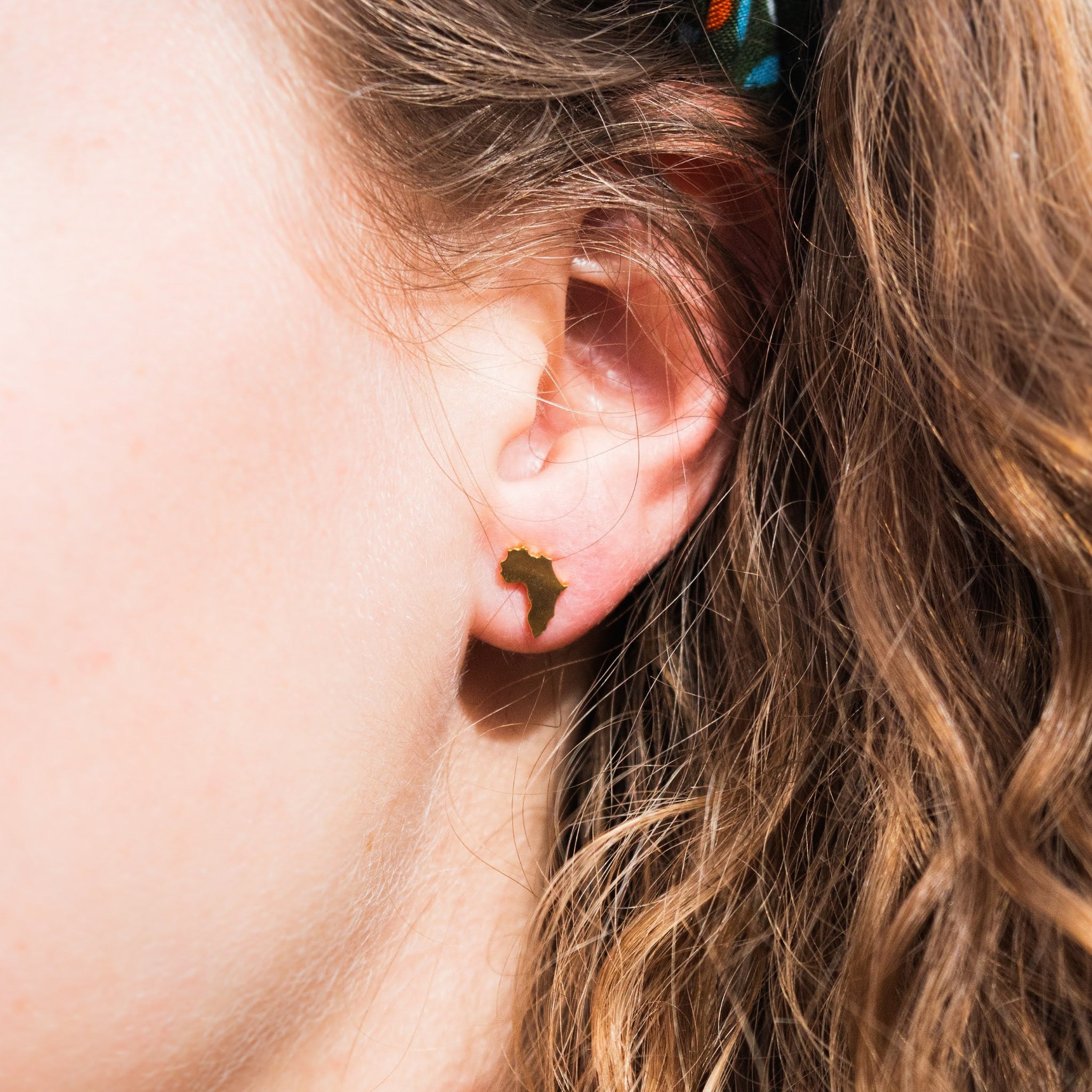 A person wearing a small brass earring shaped like the continent of Africa.