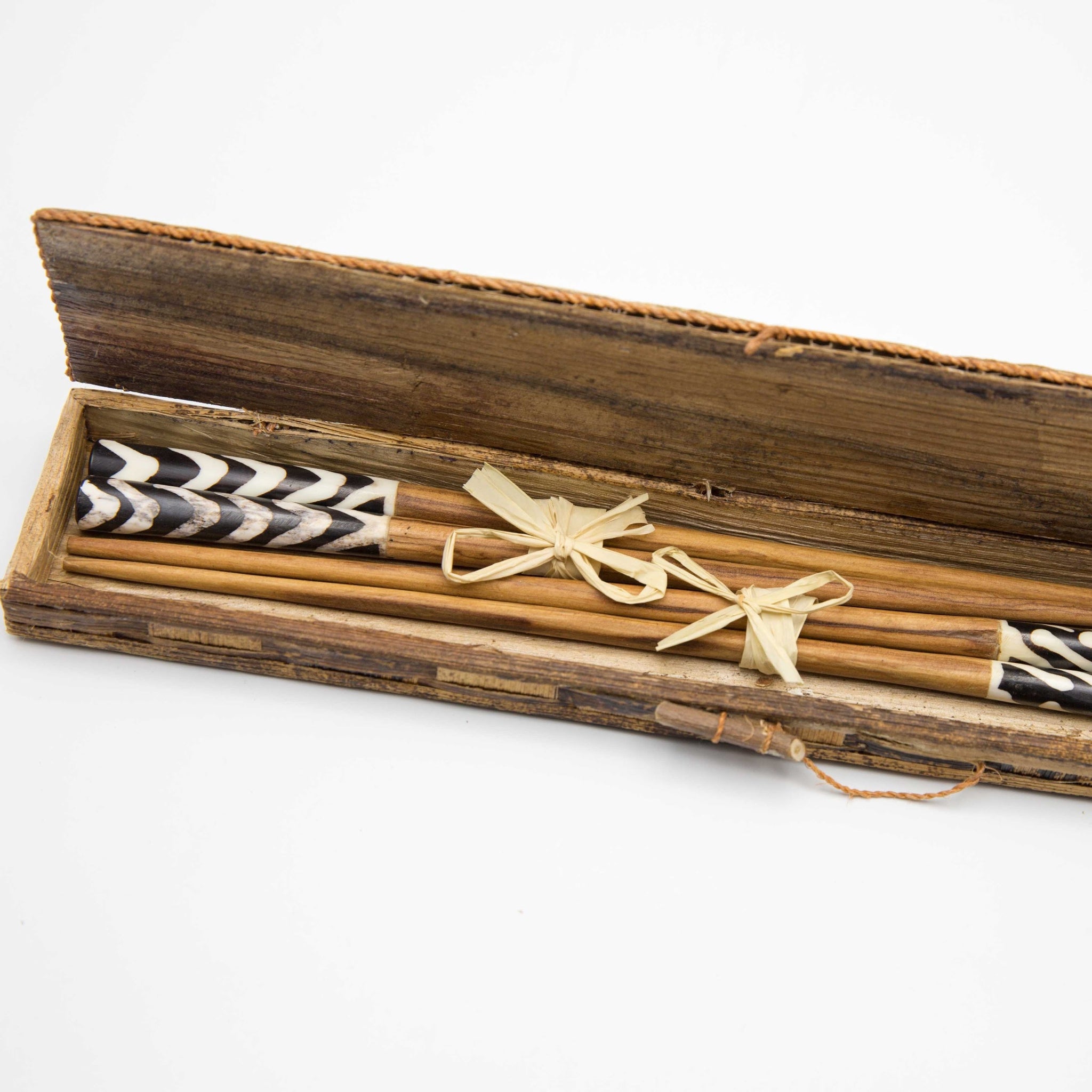 Two sets of wooden chopsticks in a rustic wooden box, tied with a light tan string. The ends of the sticks feature black and white chevron patterns.