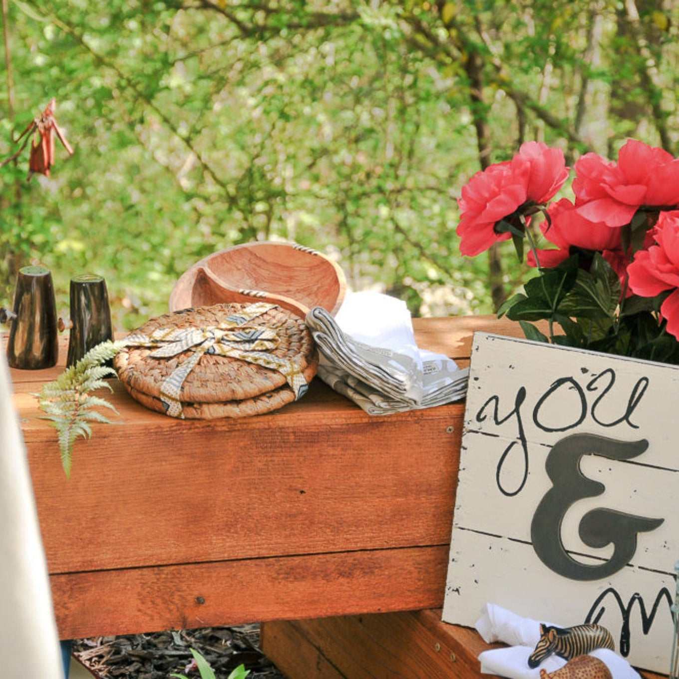 Wooden surface with woven hot plates, pink flowers, and a sign outdoors.