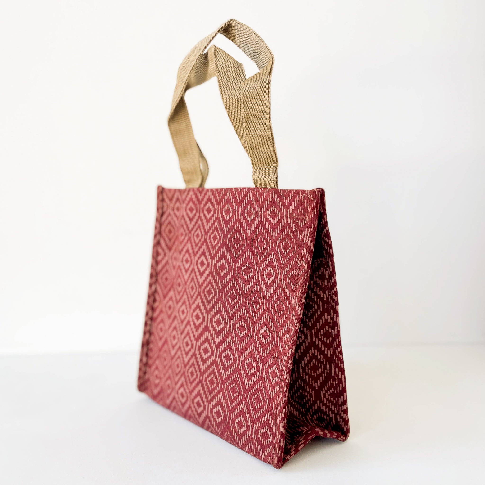 A small fabric tote lunch bag with a red and white geometric diamond pattern, featuring natural beige woven handles, shown on a plain white background.
