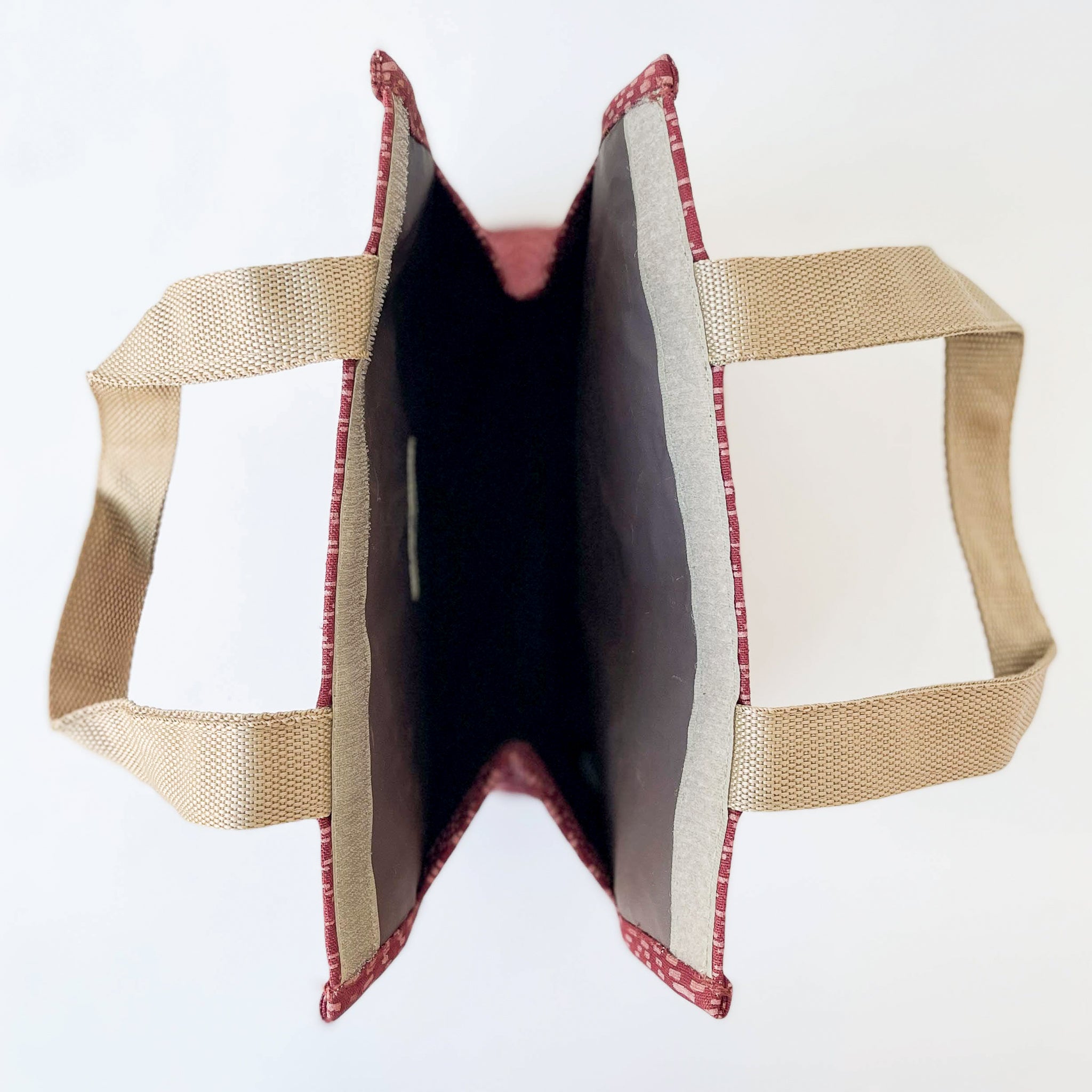 An open lunch tote insulated bag shown from above on a plain white background, with beige woven handles and a dark interior lined in red patterned fabric.