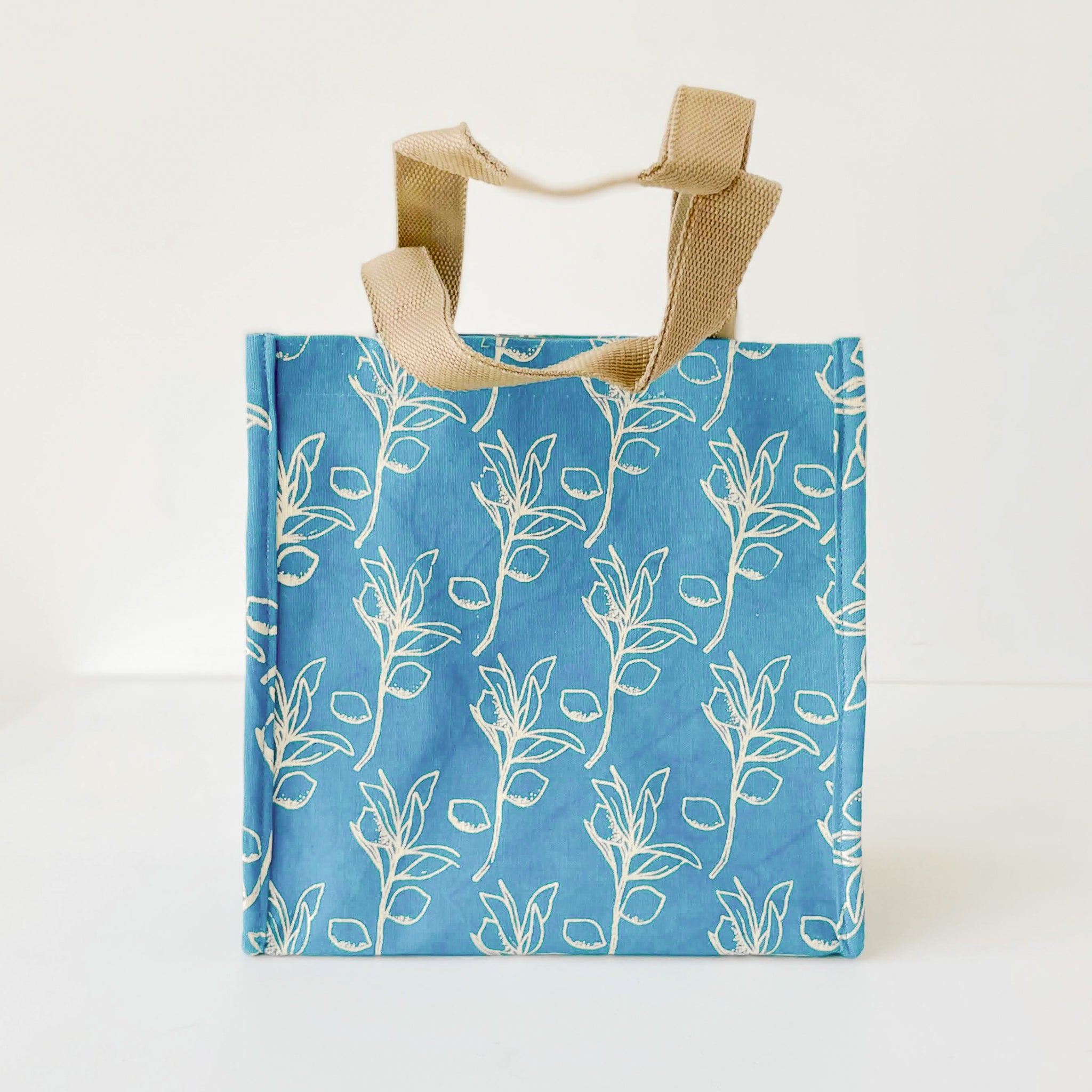 A blue fabric lunch tote bag with a cream olive leaf pattern and natural beige canvas handles, shown against a plain white background.
