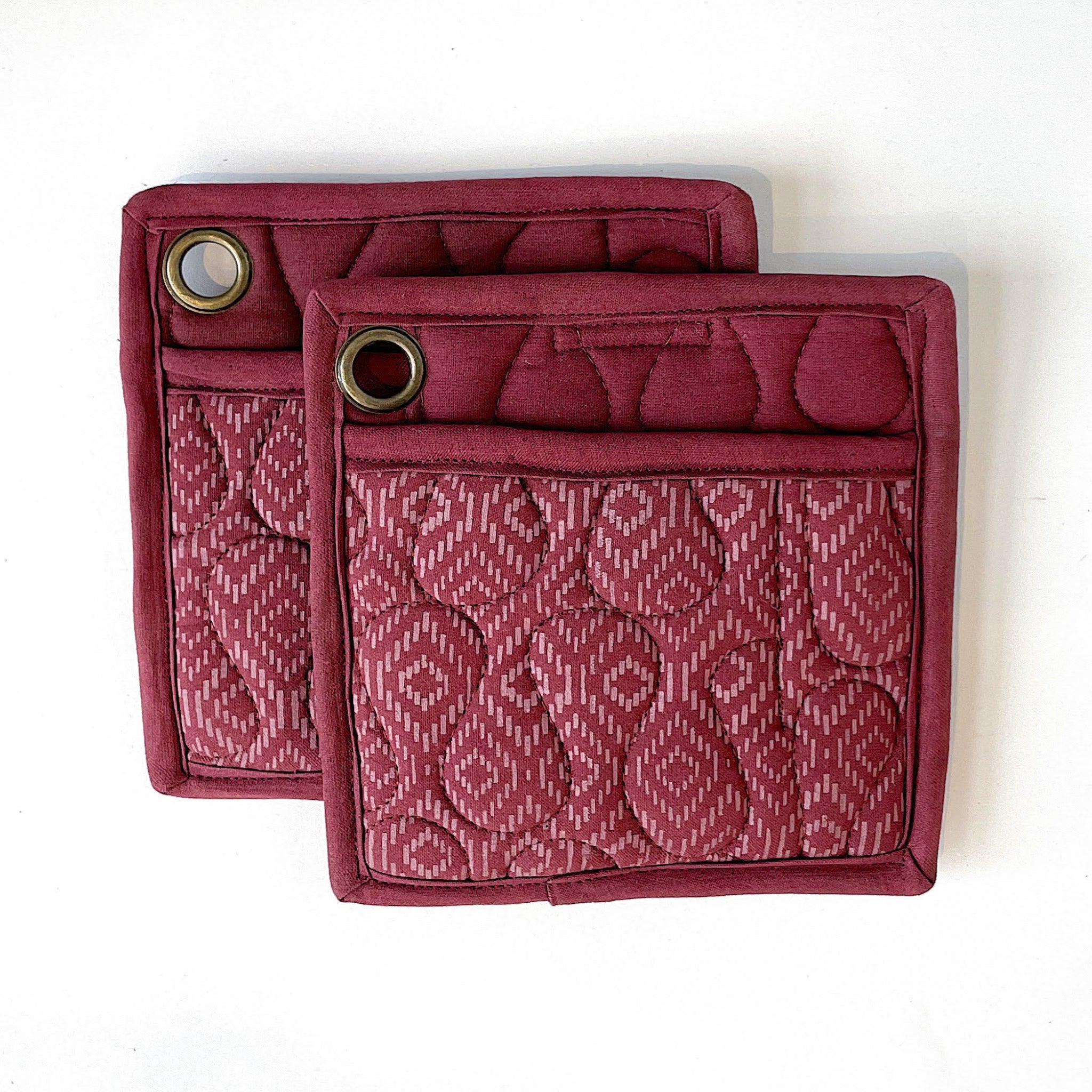 Two maroon pot holders with patterned design on a white background
