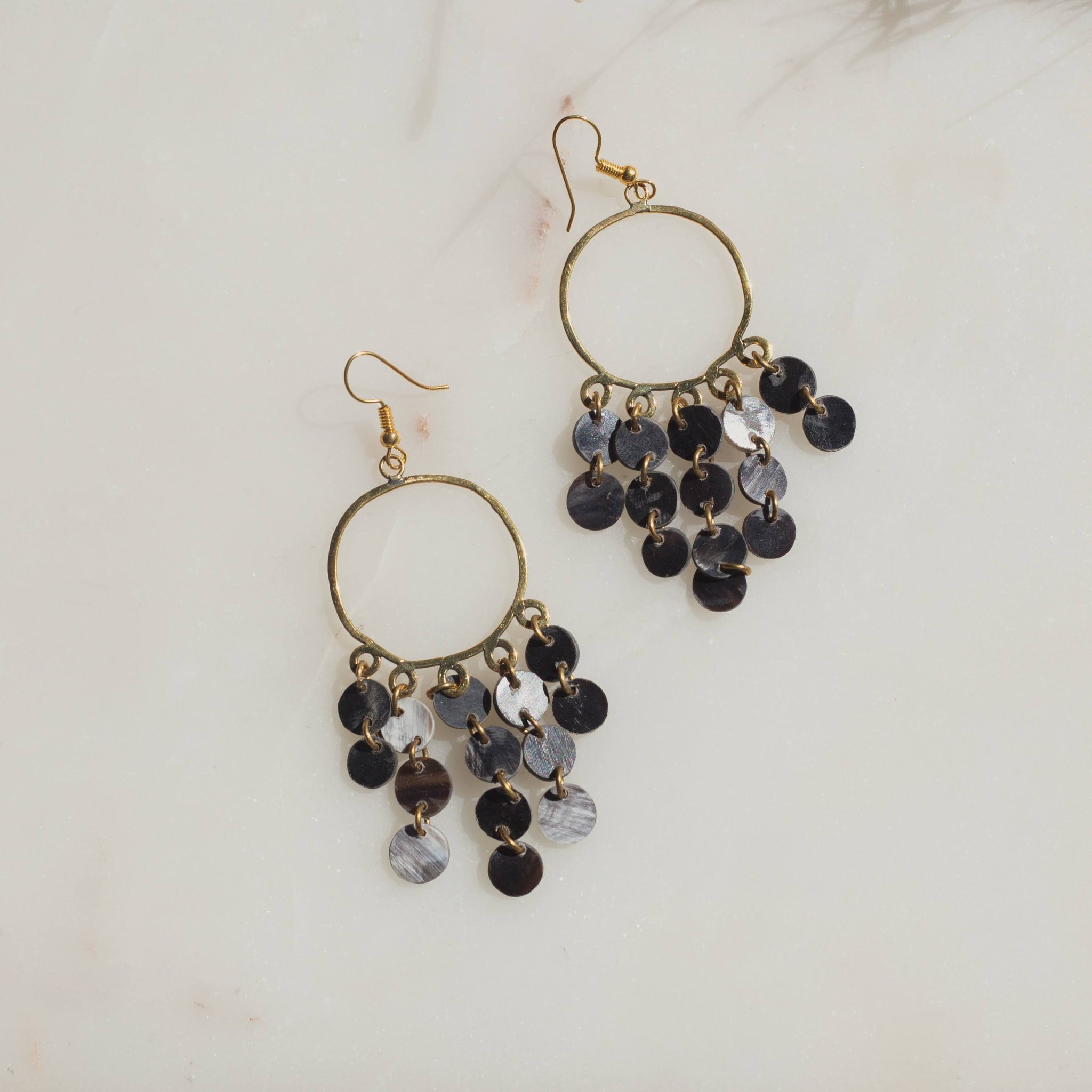 Pair of brass hoop earrings with black and gray horn drops on a light background