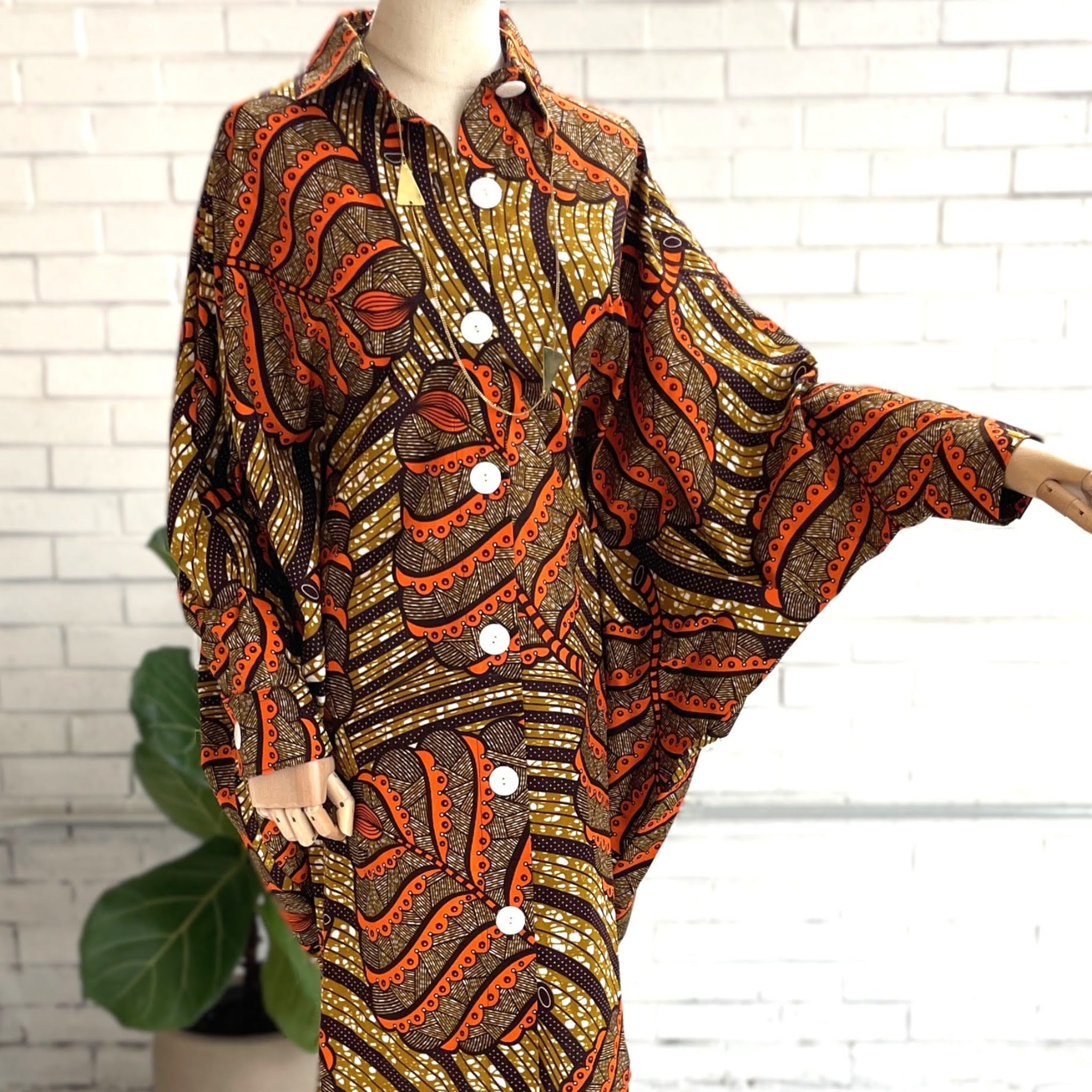 Mannequin wearing a patterned outfit with orange and brown design against a white brick wall.