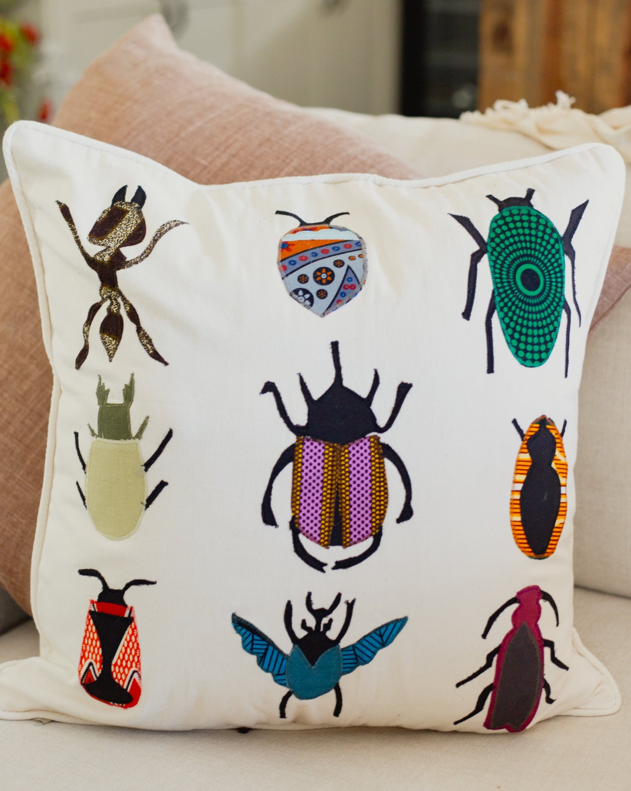 Decorative pillow with embroidered insect designs on a neutral background
