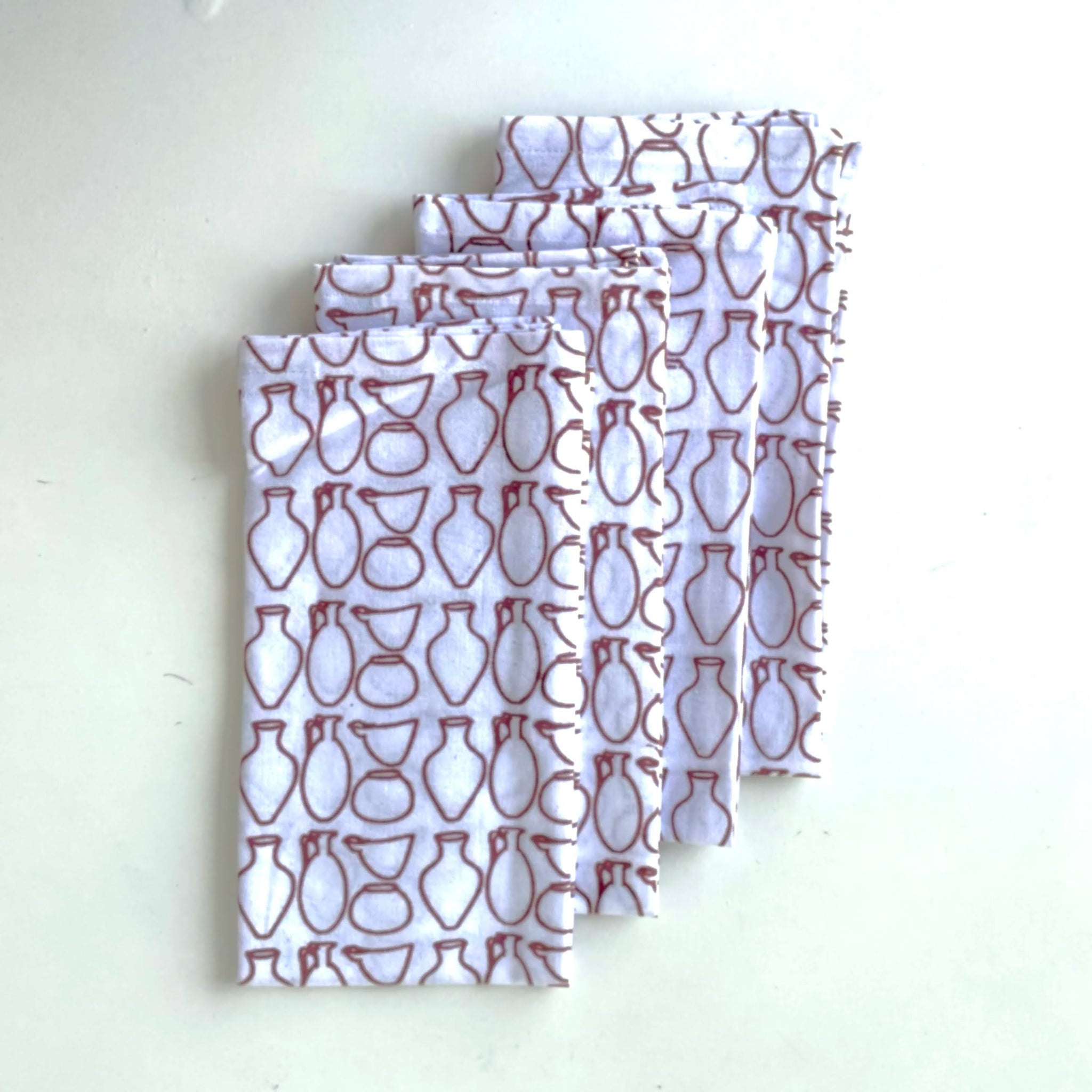 Four folded napkins with a pattern of red pottery on a white background