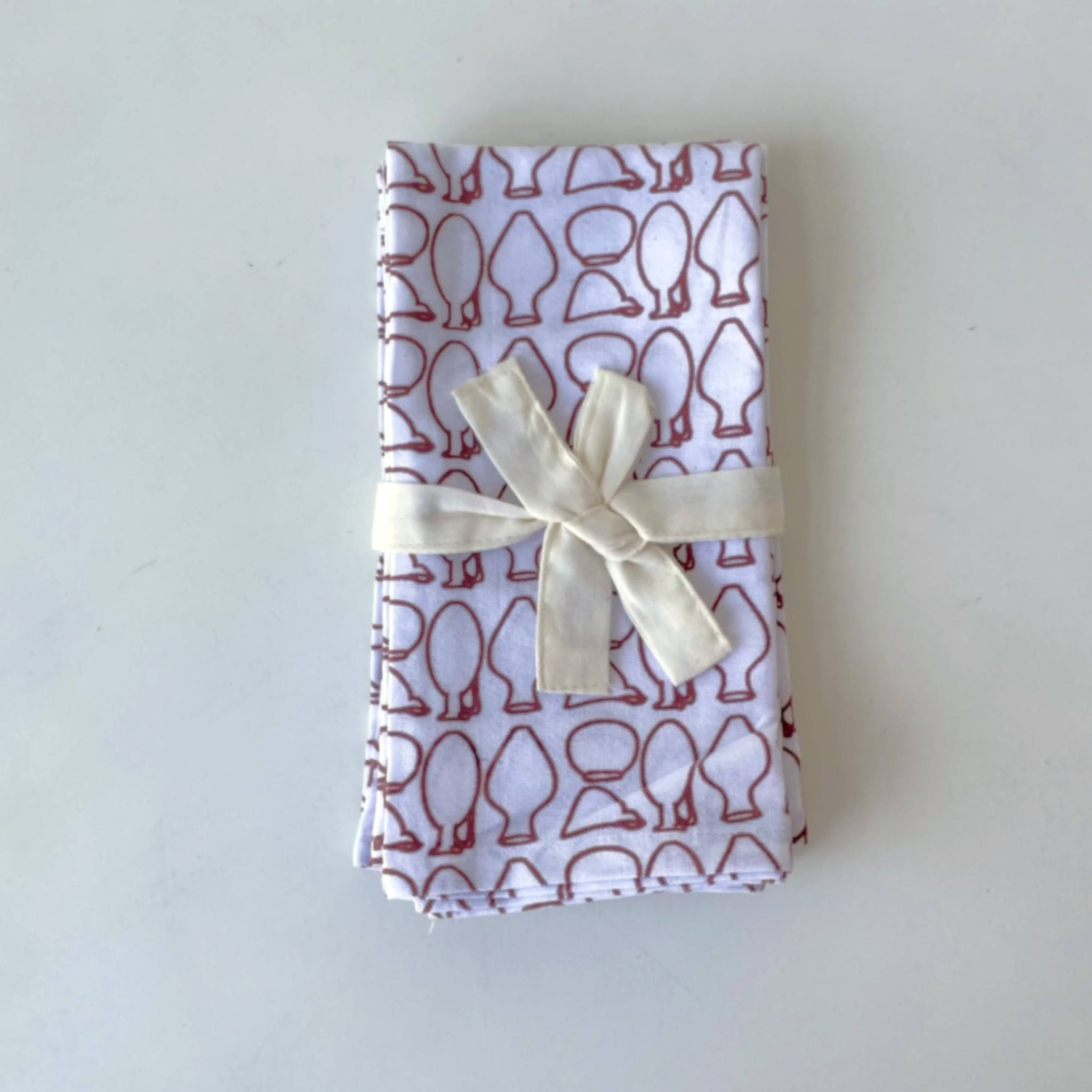 Folded napkins with a pattern of red pottery on a white background, tied with a white ribbon.