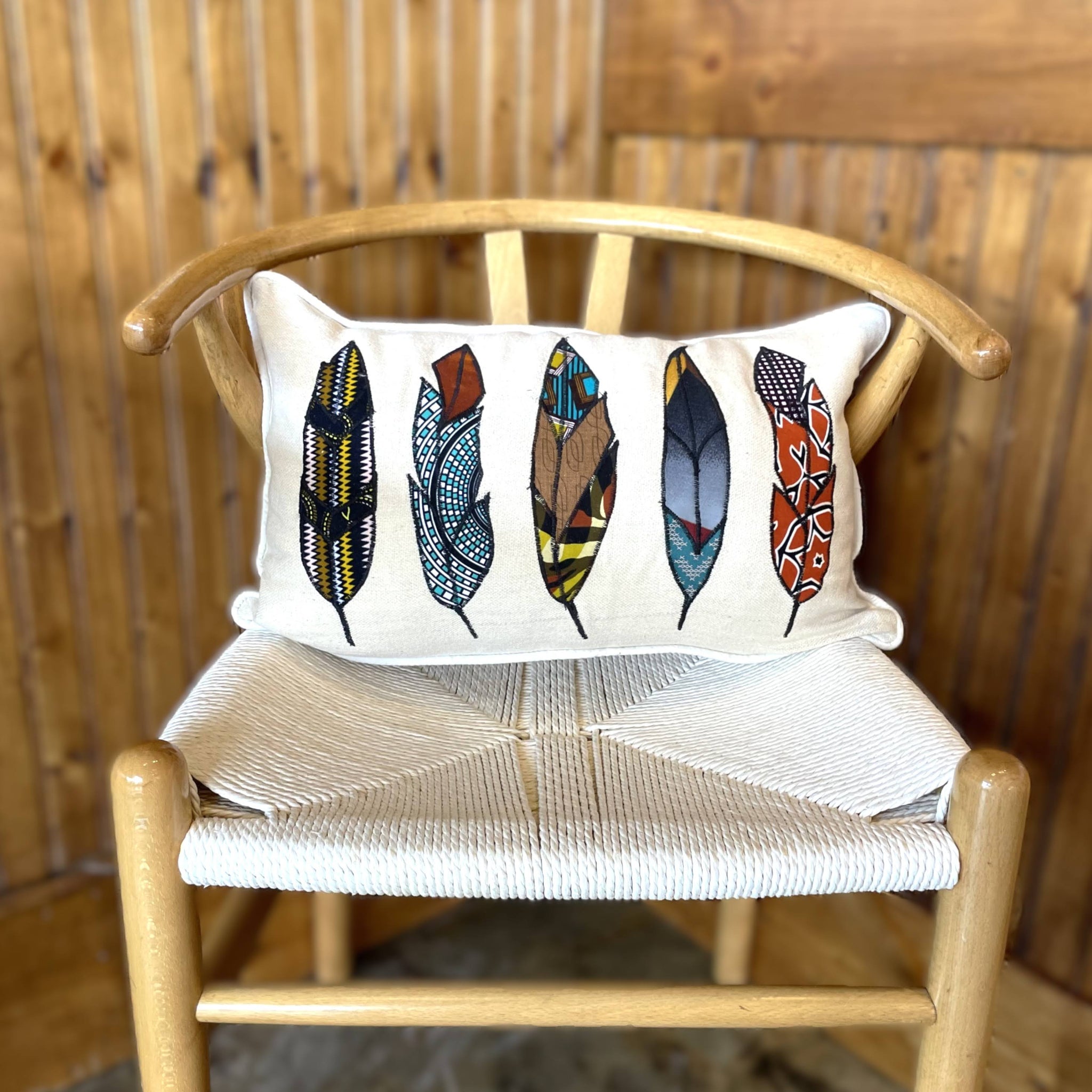 Decorative pillow with feather design on a wooden chair against a wooden wall.