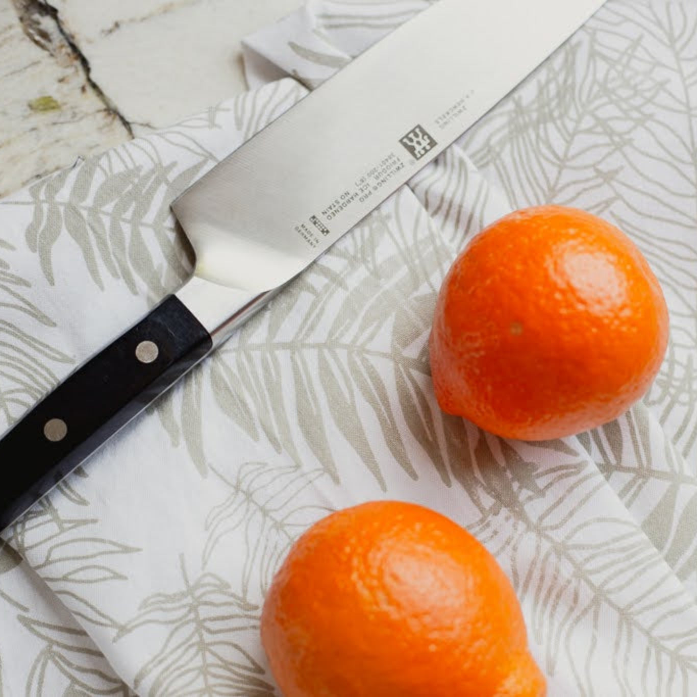 Two oranges on a fern-patterned dish towel with a knife.