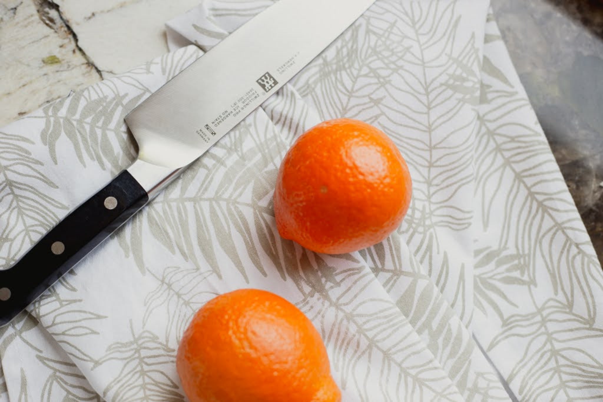 Two oranges on a fern-patterned dish towel with a knife.