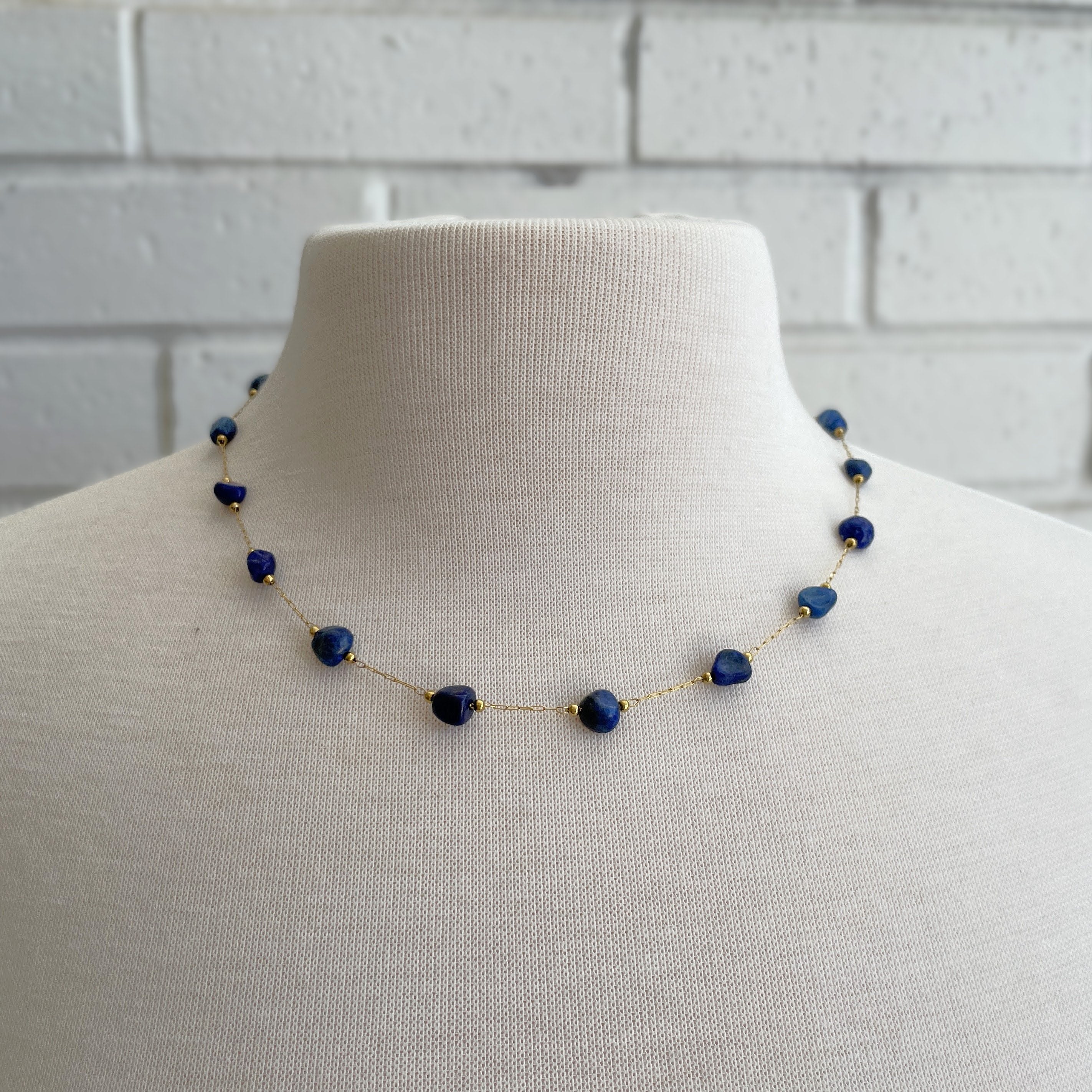 Necklace with blue beads on a mannequin against a white brick wall background