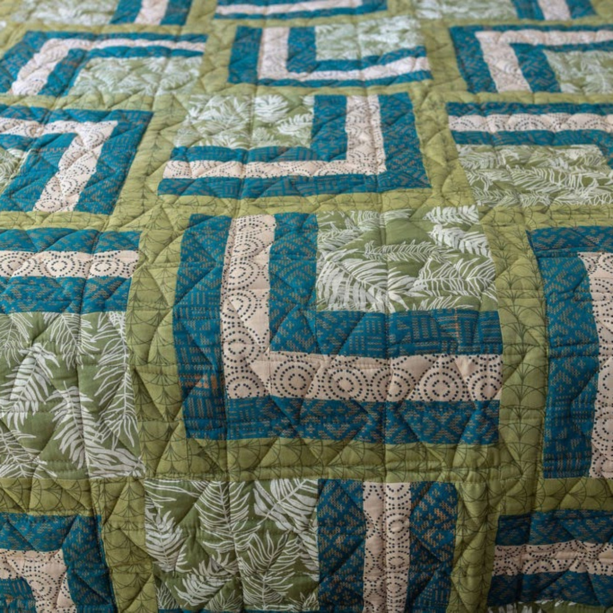 Detail of a geometric and botanical quilt in green, teal, and cream.