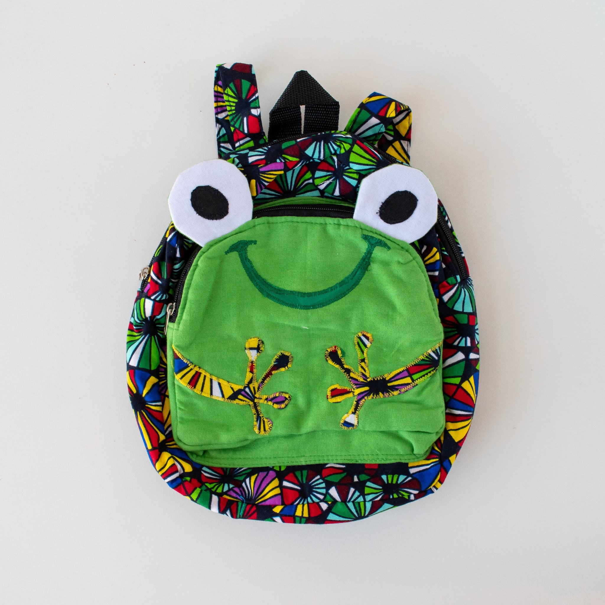 Colorful children's backpack designed like a frog on a white background