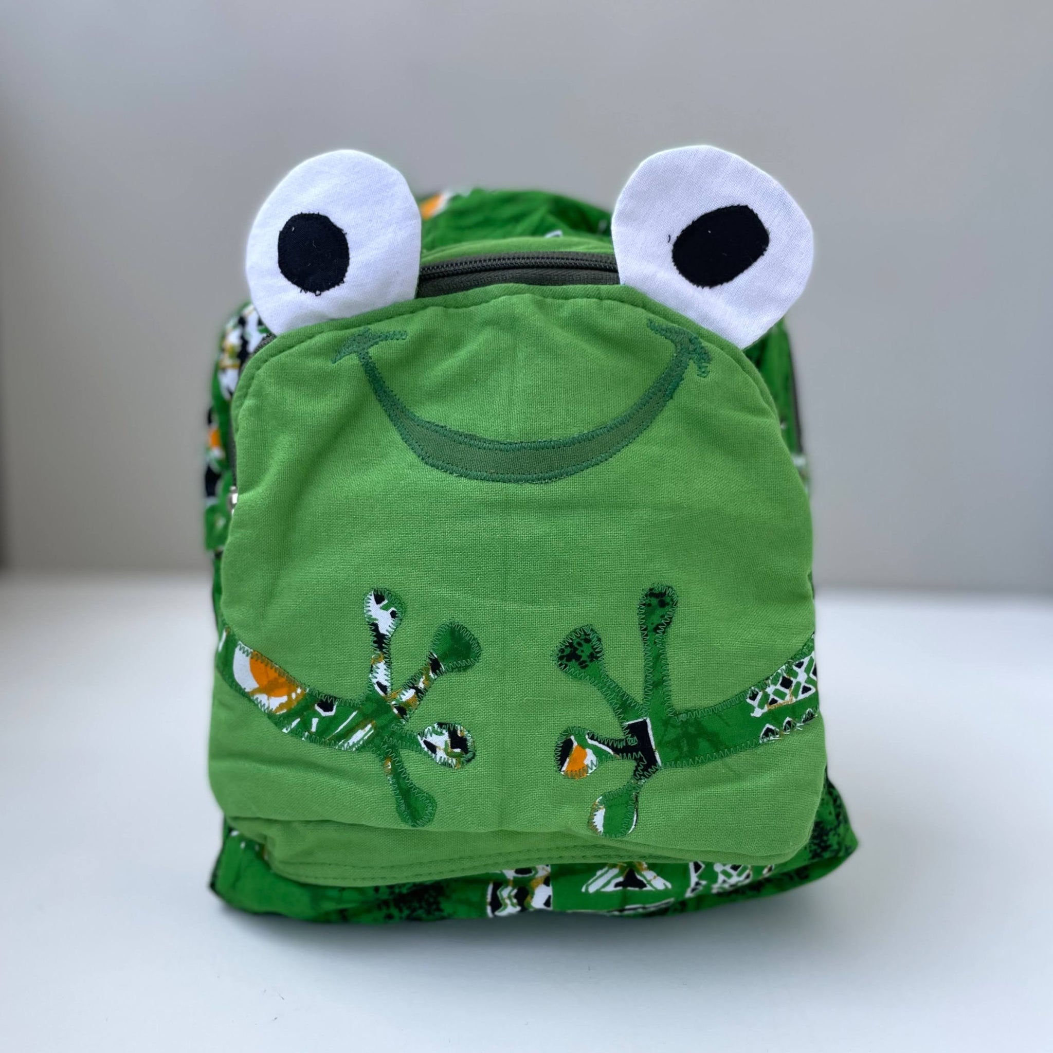 Green frog-themed backpack with white eyes on a light background