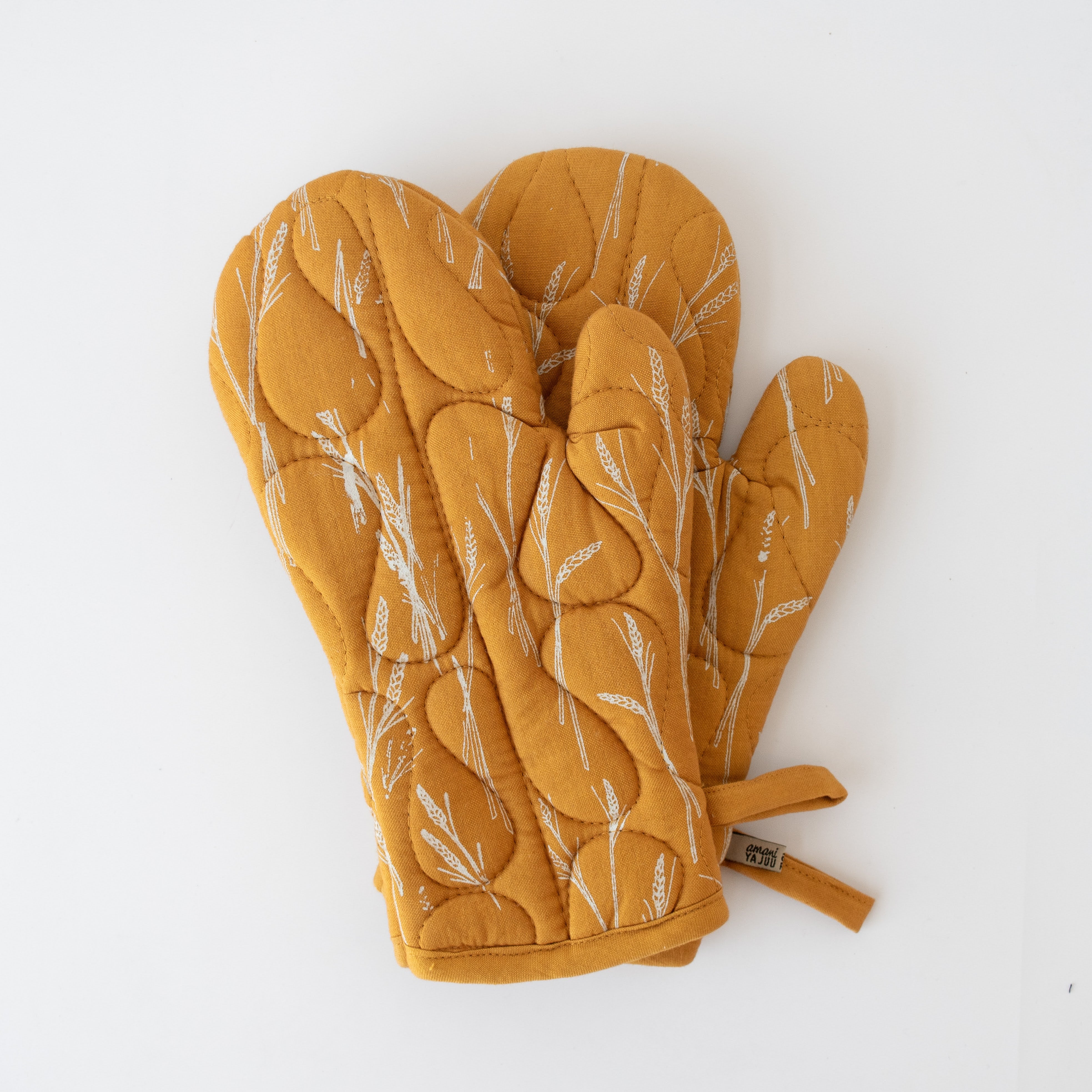 Pair of mustard yellow oven mitts with wheat pattern on a white background