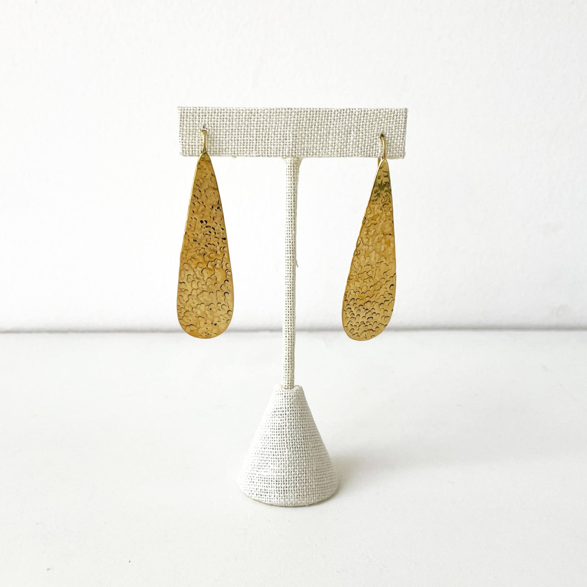 Gold teardrop earrings on a white stand against a white background