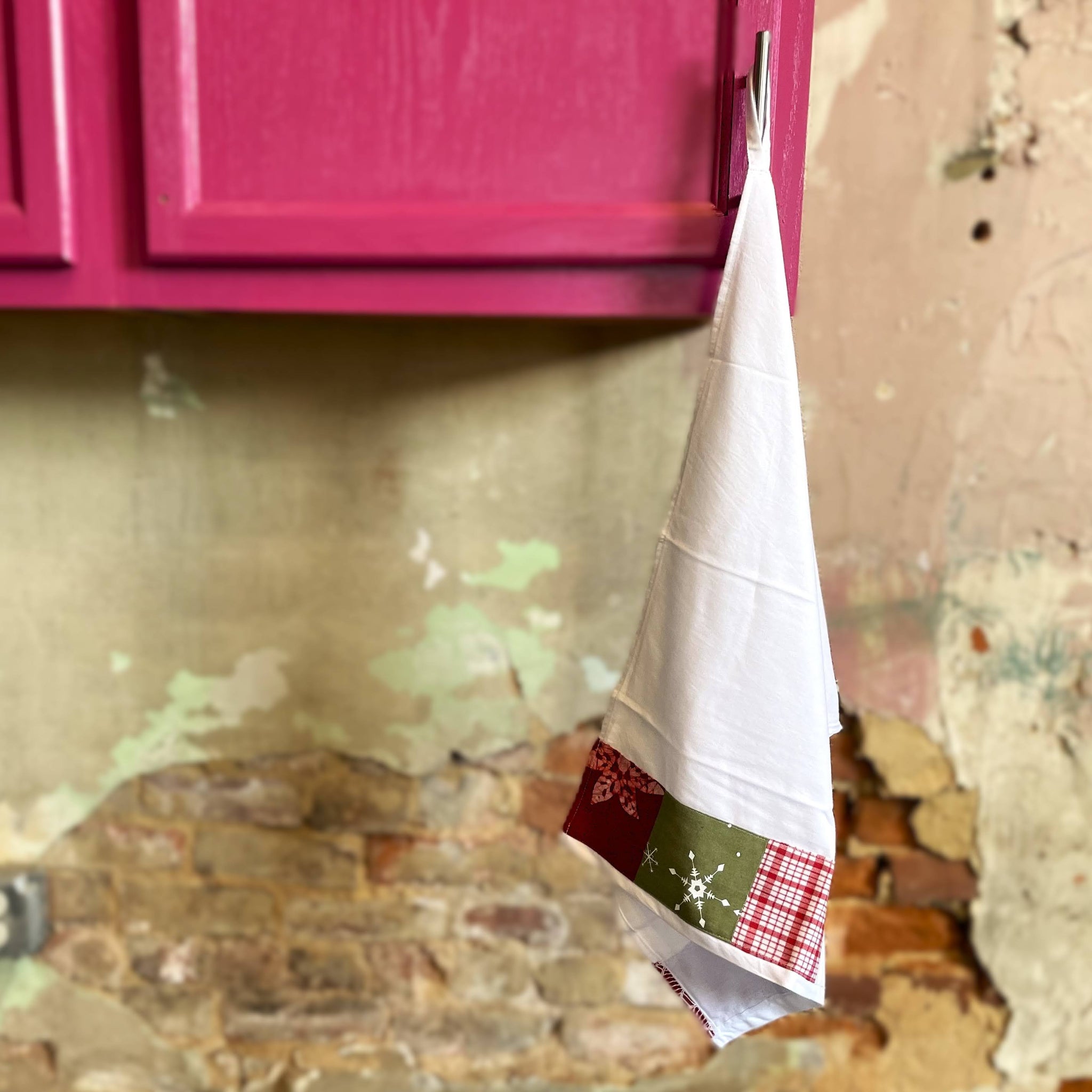 White kitchen towel with red and green pattern hanging from a pink cabinet.