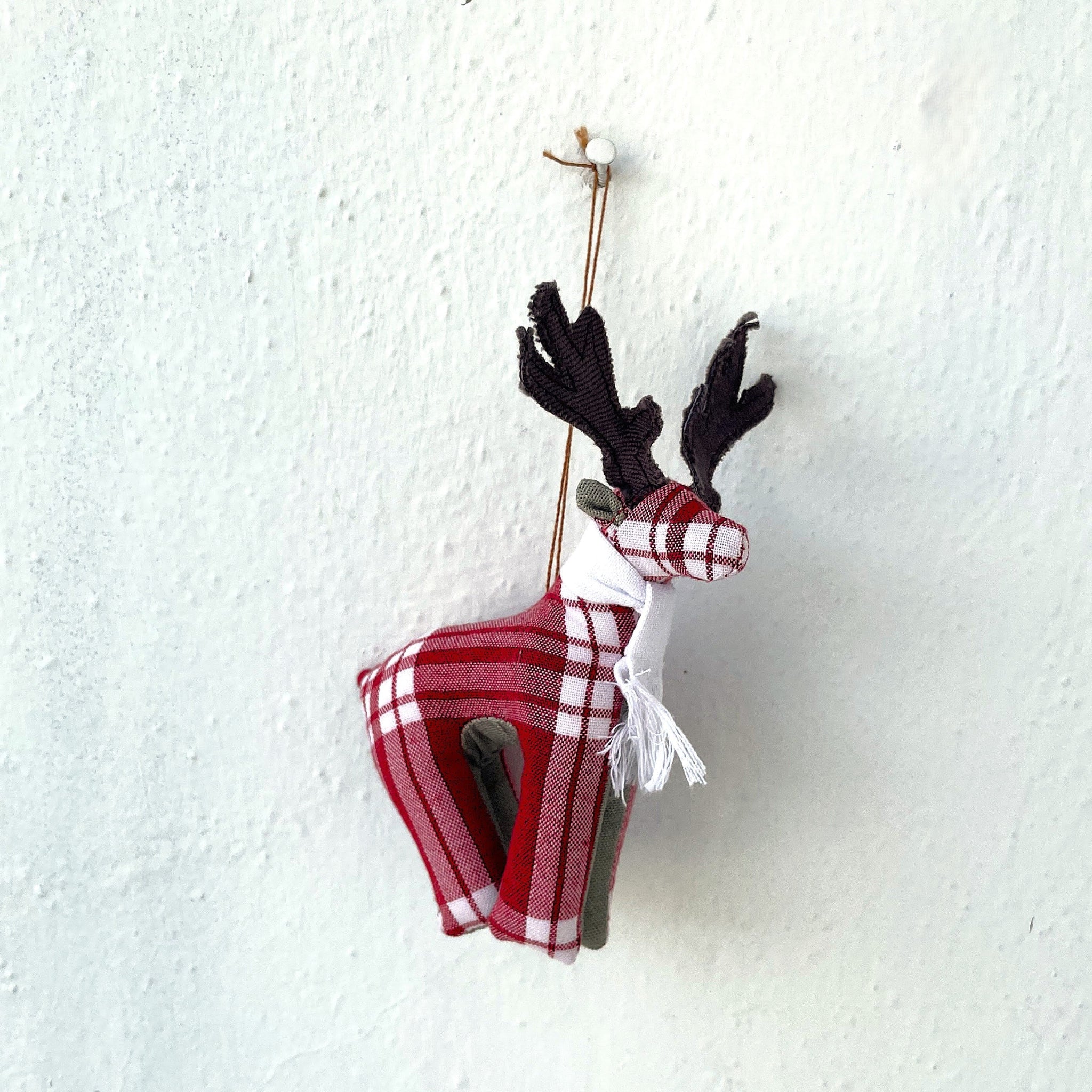 Red and white plaid reindeer ornament hanging on a textured white wall.